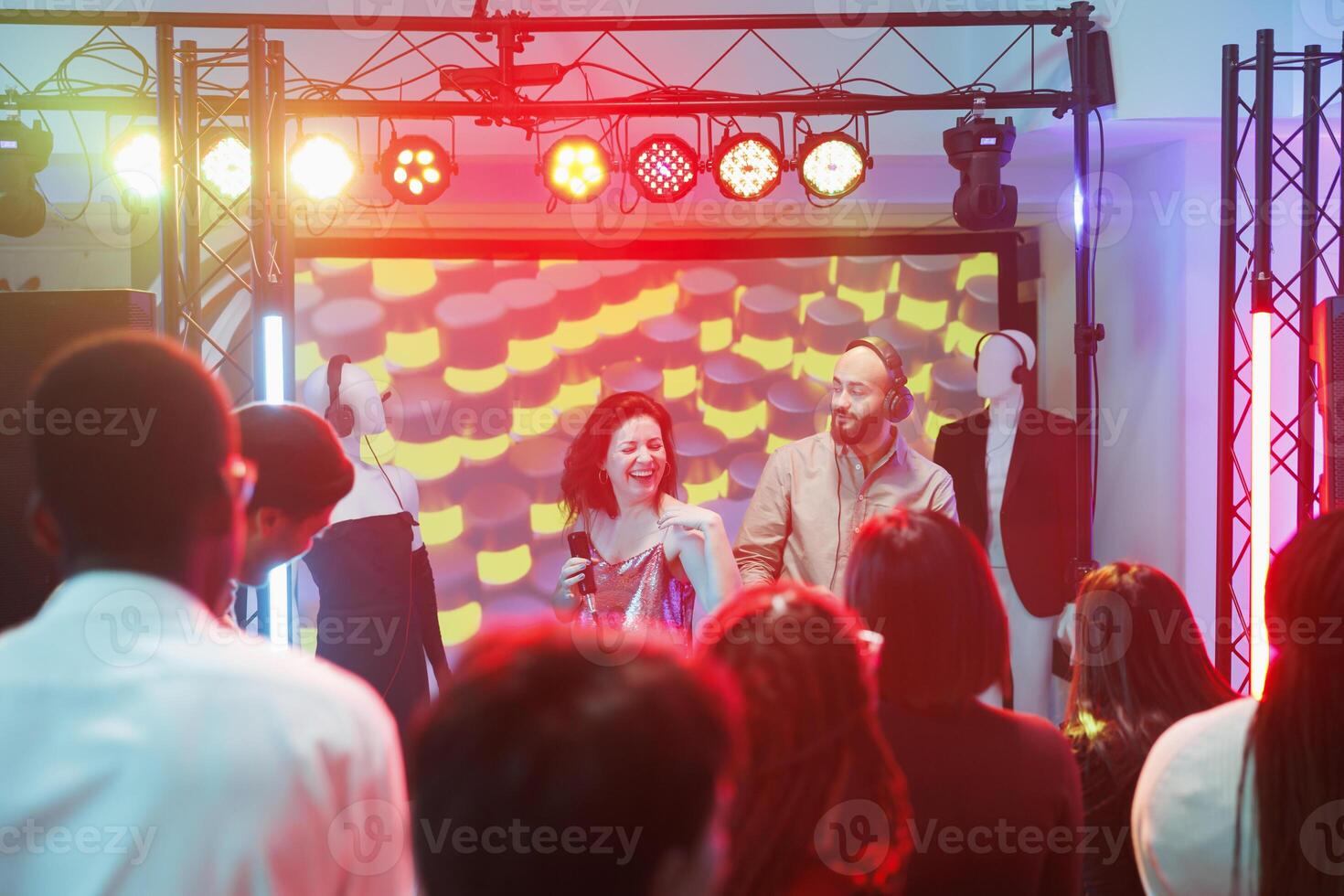 Singer and dj band performing on stage while crowd clubbing at dance party in club. People having fun on dancefloor while musicians playing at electronic music festival in nightclub photo