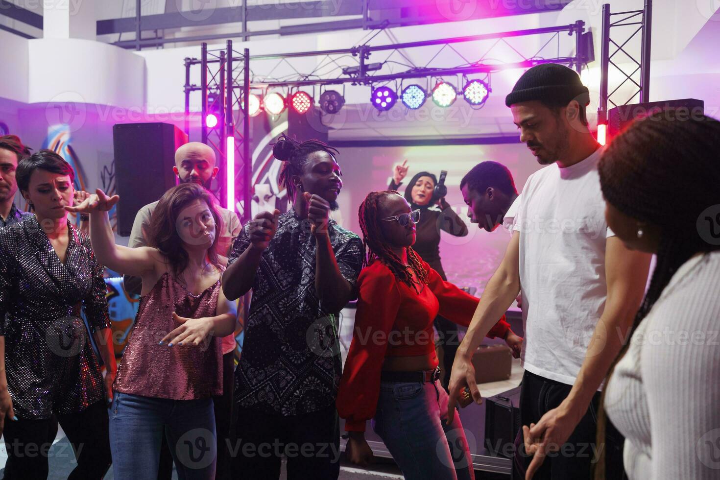 Cheerful young people dancing together at social gathering in nightclub. Happy men and women crowd clubbing and partying on dancefloor while attending discotheque in club photo