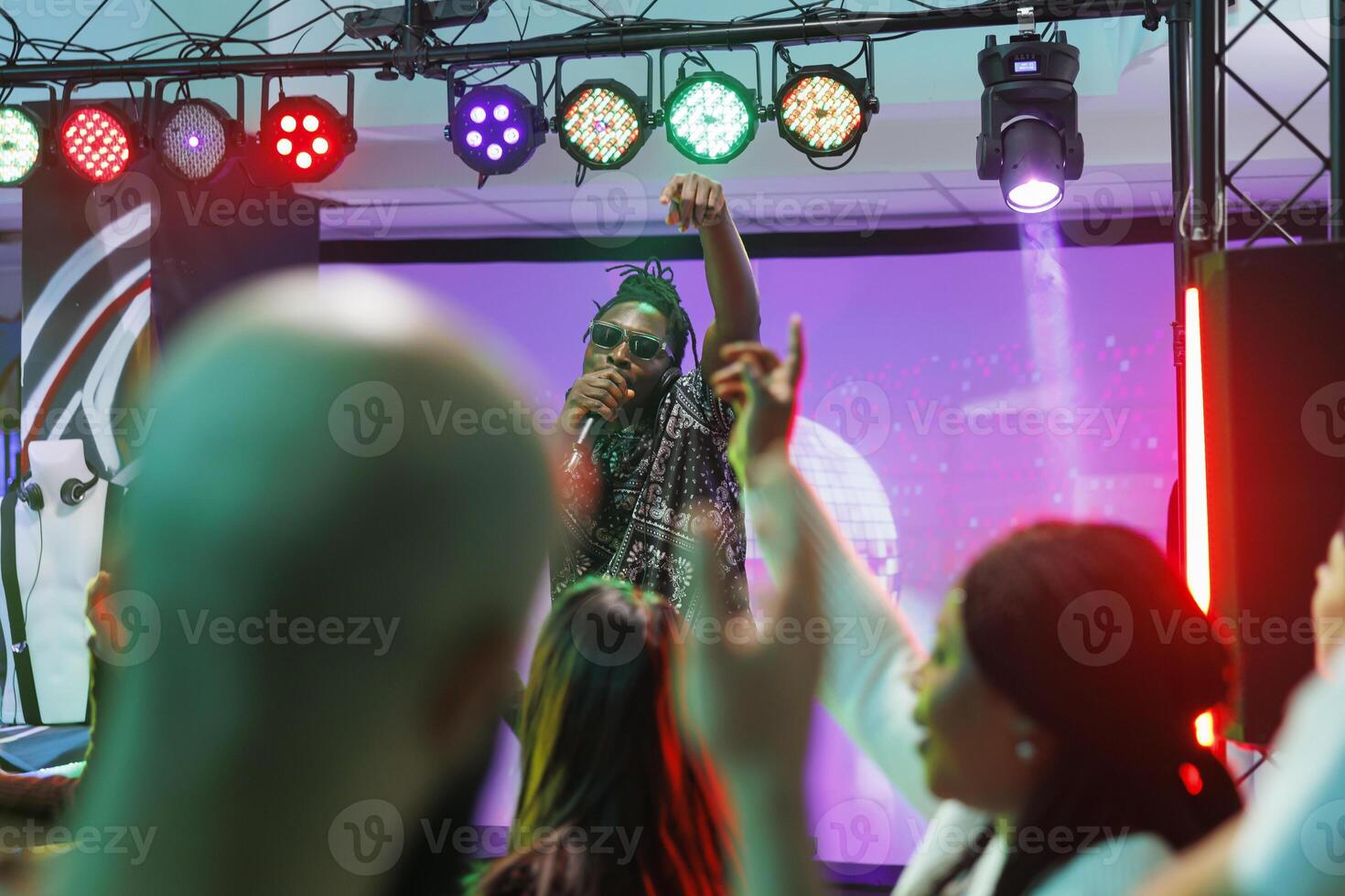 African american musician rapping on stage while crowd dancing at concert in nightclub. Cool dj singing in microphone while clubbers partying on dancefloor at performance in club photo