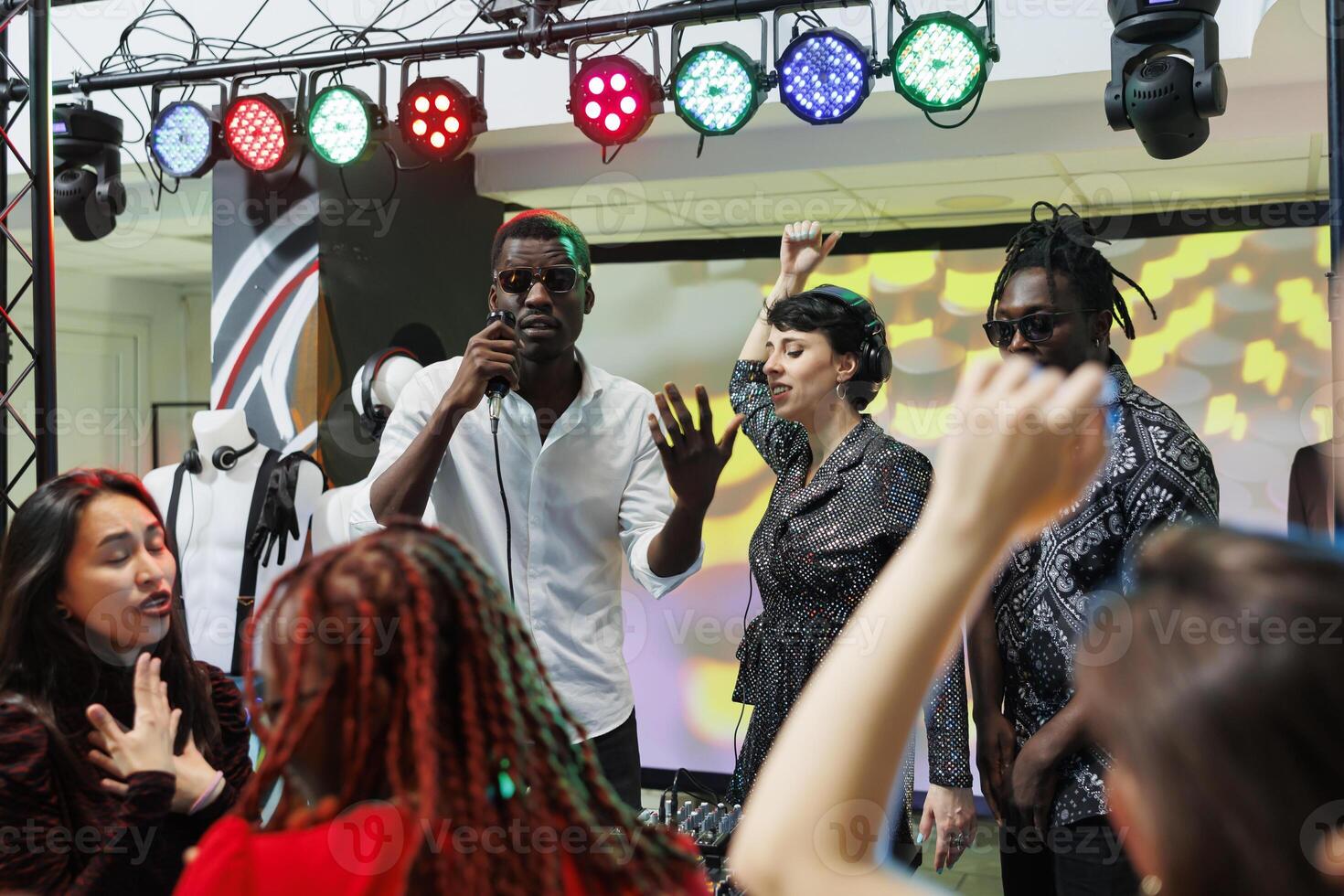 Band performing on stage with spotlights while crowd cheering and clubbing on nightclub dancefloor. Musicians singing and playing at electronic music festival live concert in club photo