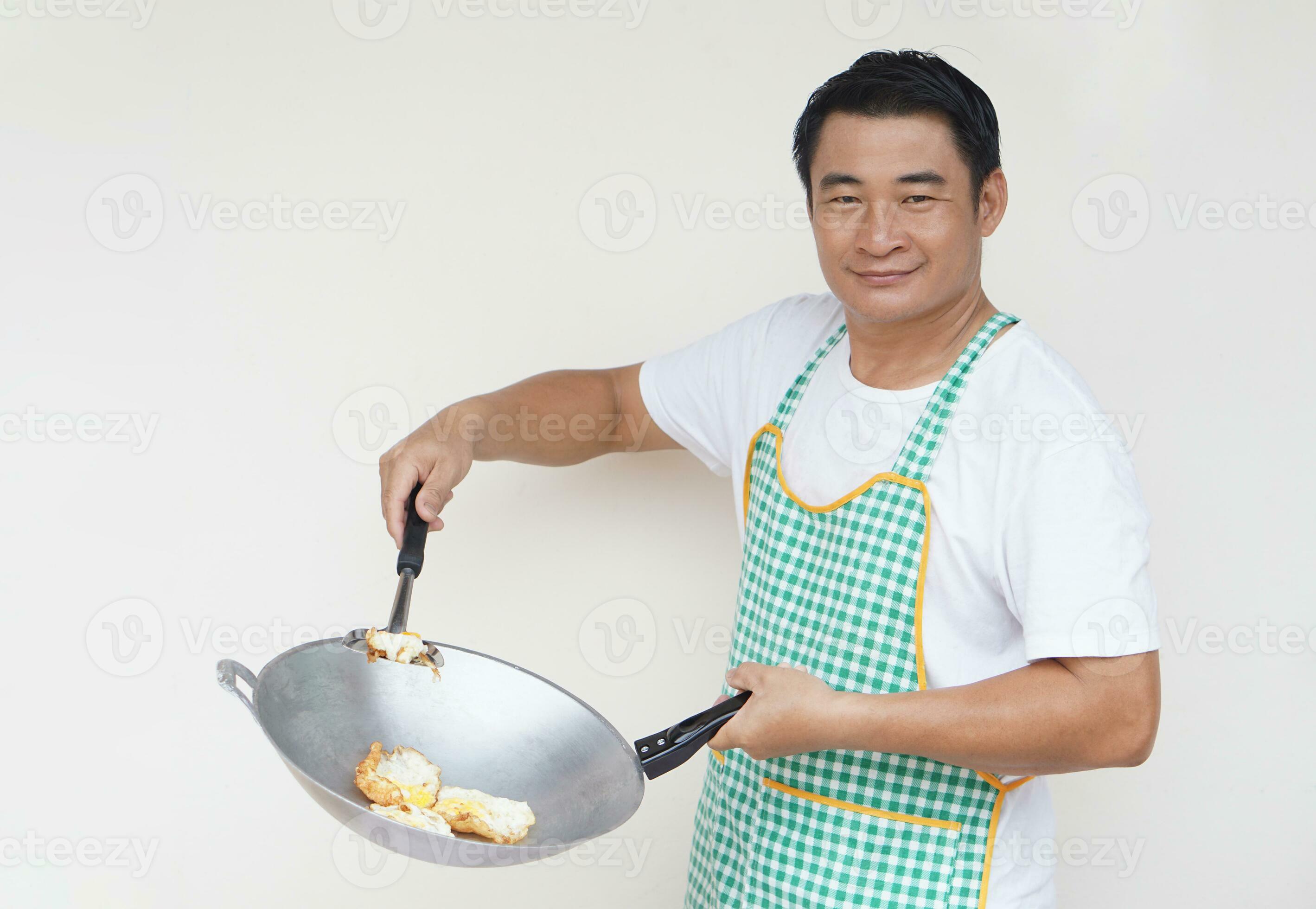 Handsome Asian man chef is cooking fried eggs, wears white shirt and