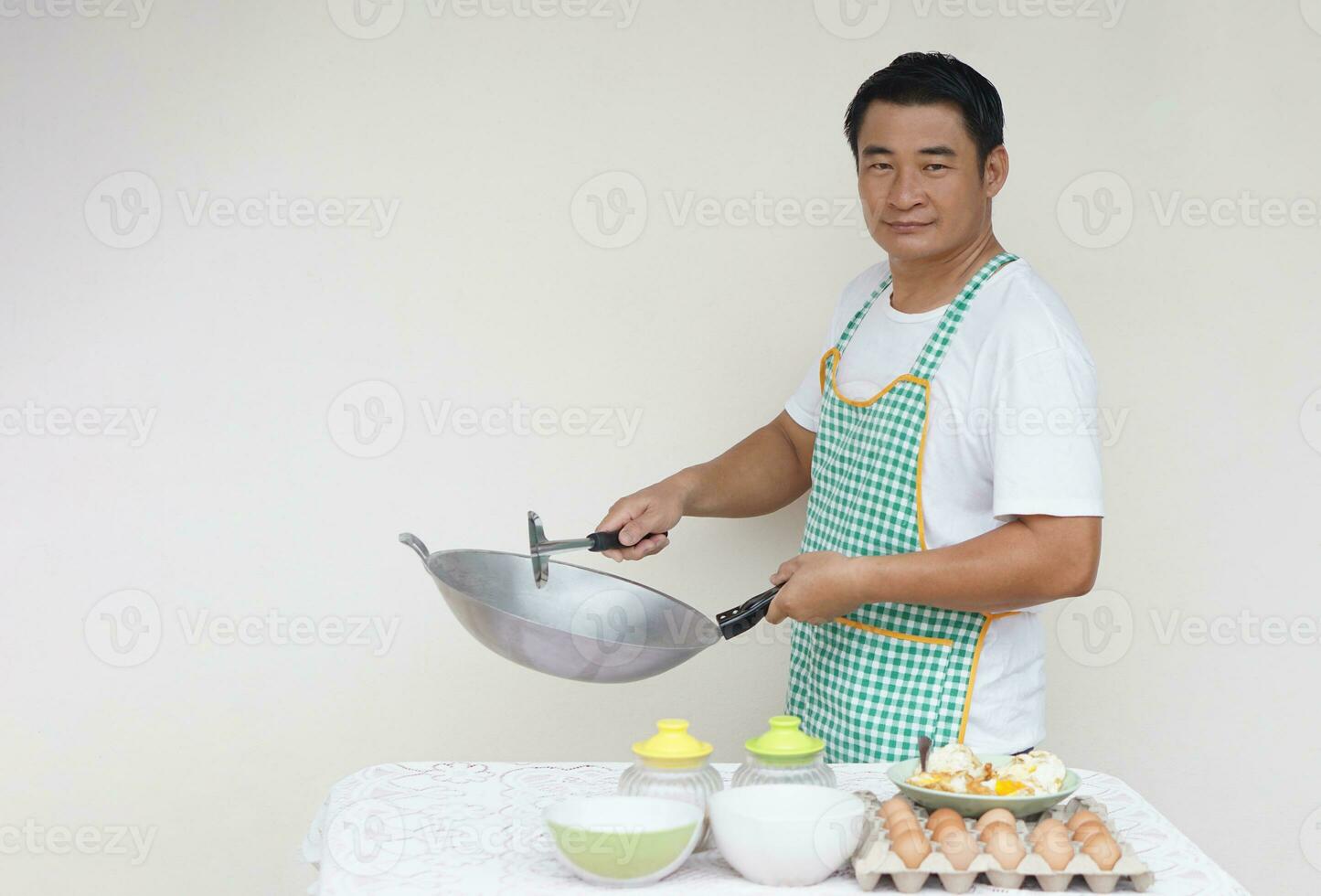 Handsome Asian man chef is cooking fried eggs, wears white shirt and