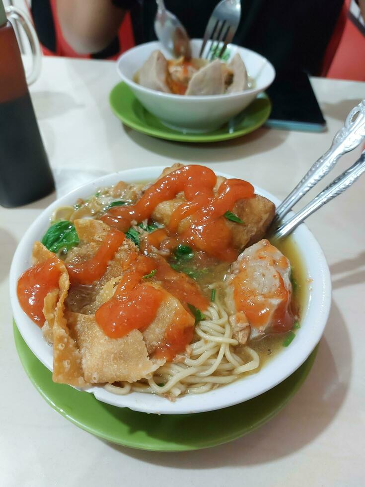 Complete Mie ayam or Mie Yamin or Yamin Noodle with chicken meat, vegetable, Pangsit Goreng, Pangsit rebus and meat ball on white plate photo