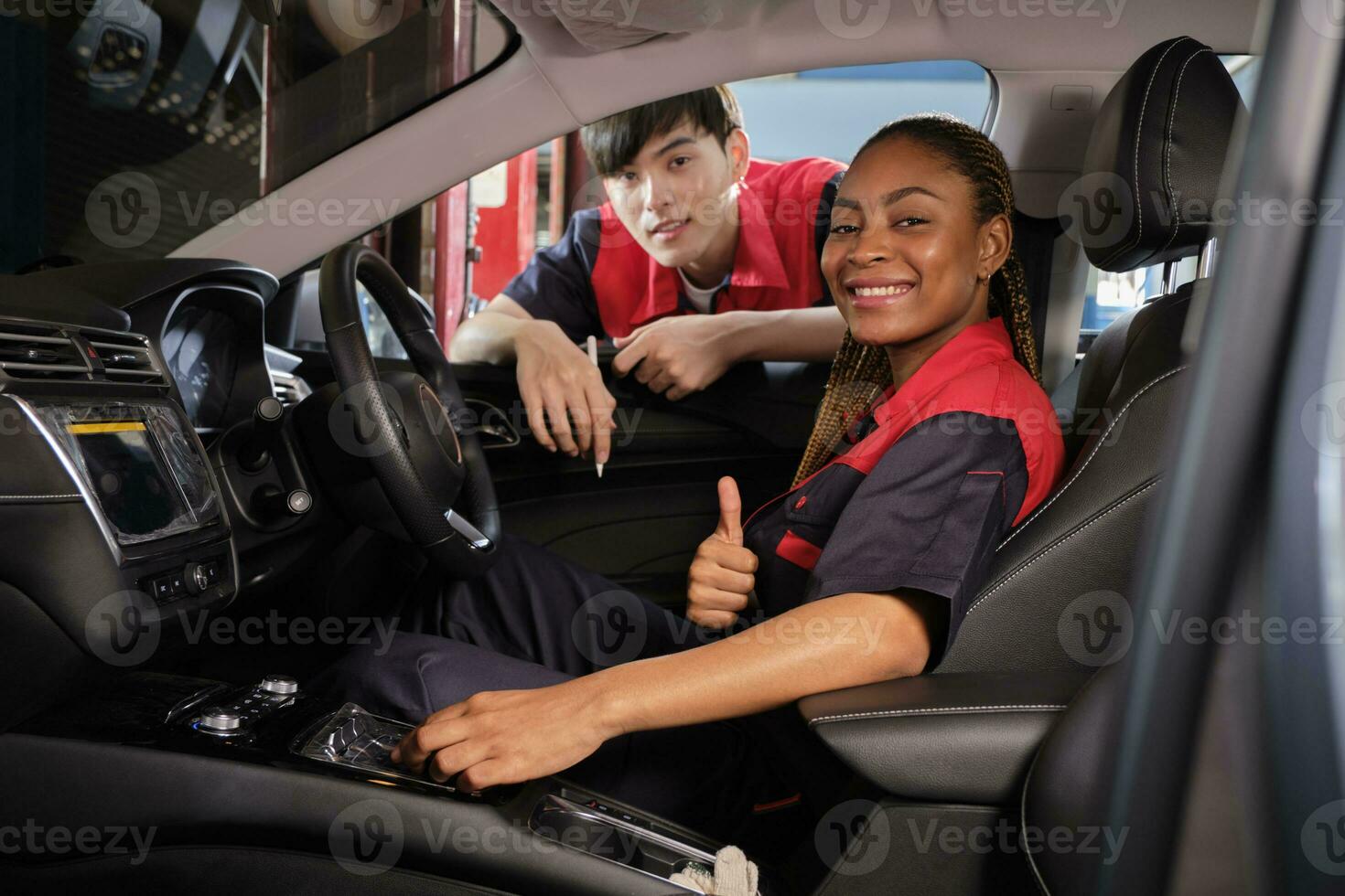 Young Black female automotive mechanic technician and partner check maintenance list in car interior at garage with smiles. Vehicle service fix and repair works, industrial occupation business jobs. photo