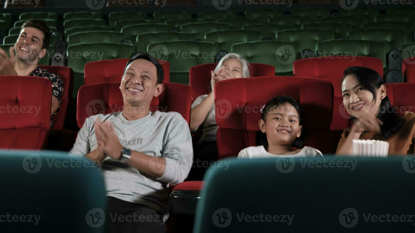 Various people in theater. Asian family, Kid, and parent audiences enjoy watching cinema and applauding together on movie stage, entertainment lifestyle with film art shows, happy and cheerful smiles. photo