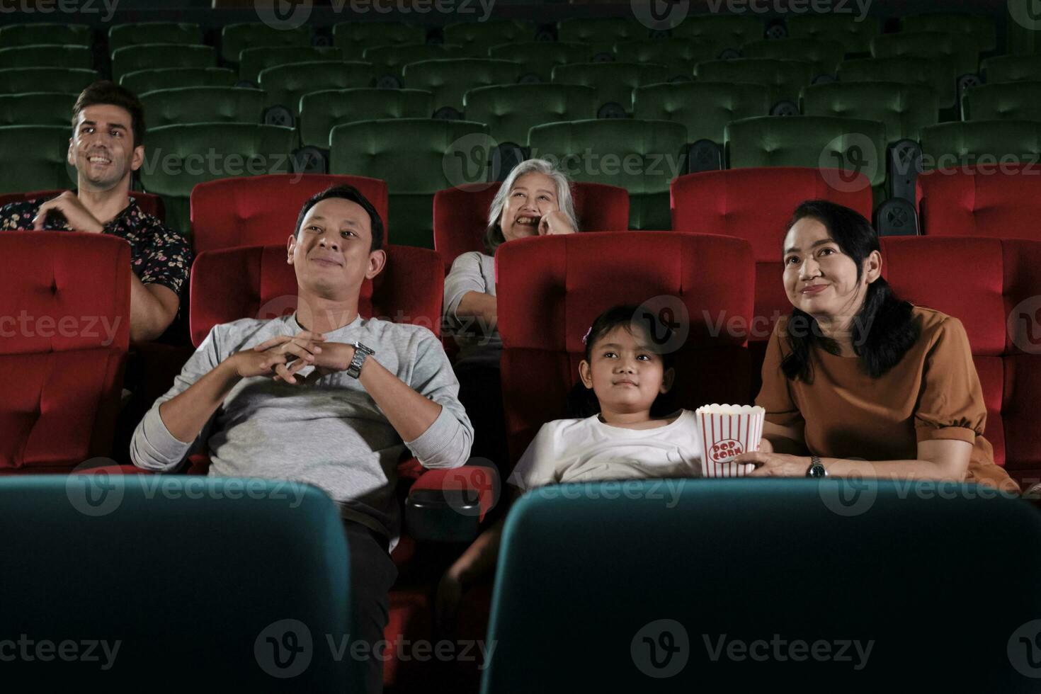 Asian family audience enjoys watching cinema together at movie theaters. Kid and parents have indoor entertainment lifestyle with performance art shows, happy and cheerful with popcorn and a smile. photo