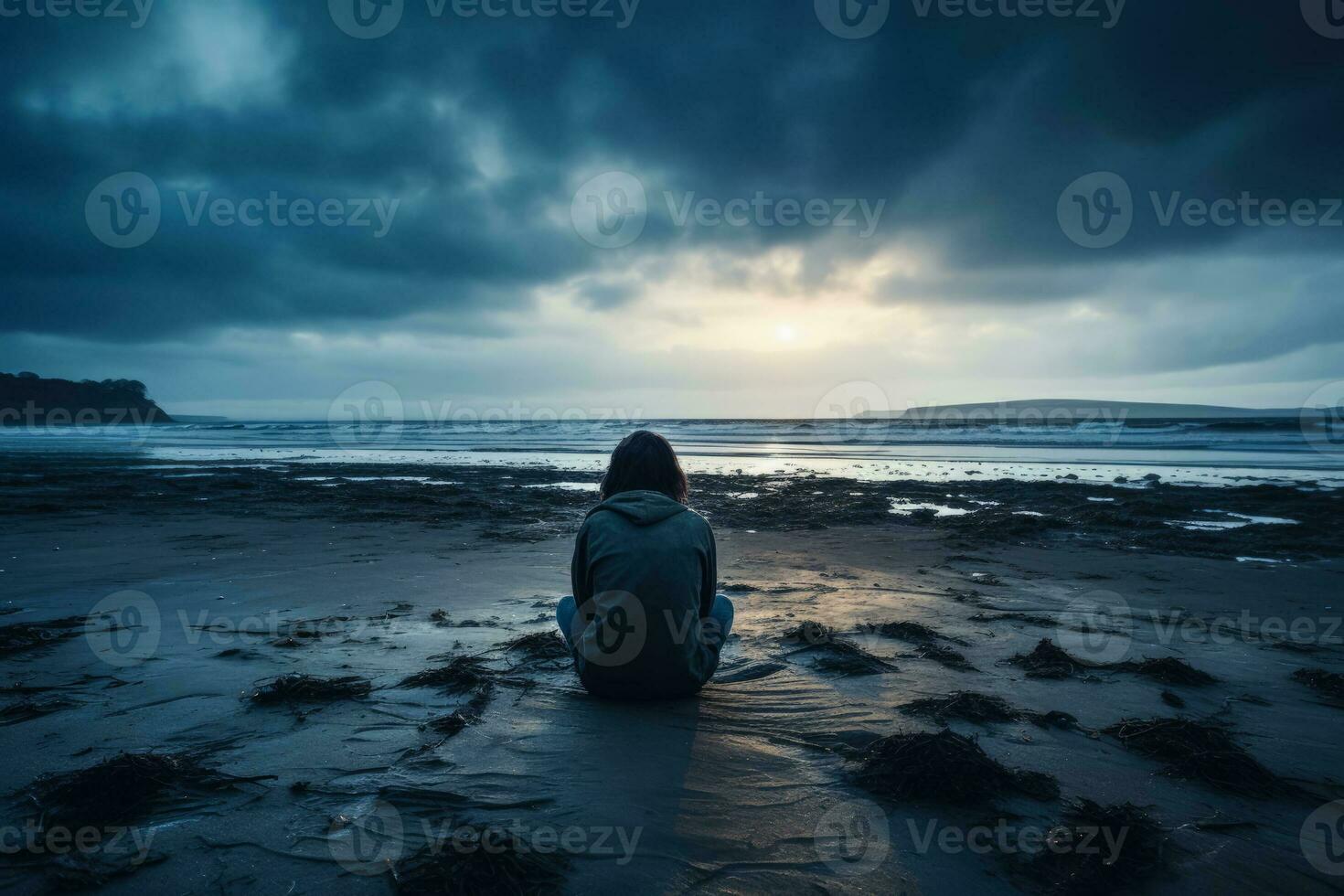 Distressed individual sitting alone displaying sadness on an eerily quiet beach photo