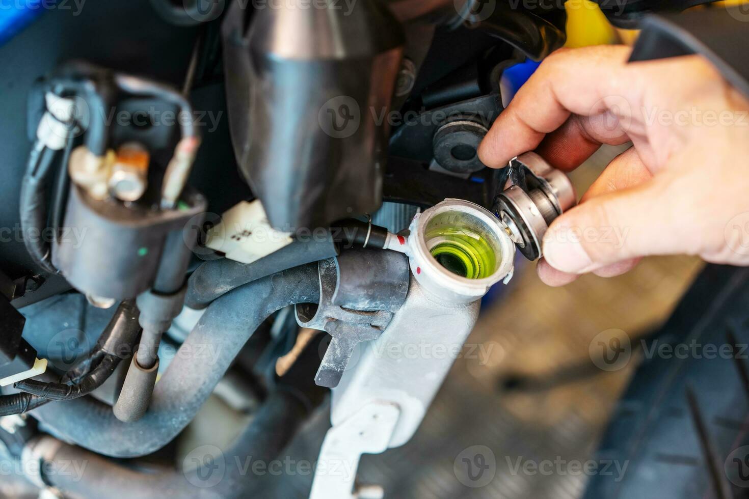 Biker removing the cap from a cold radiator and check coolant fluid levels in motorcycle at garage, motorcycle maintenance and repair concept. photo