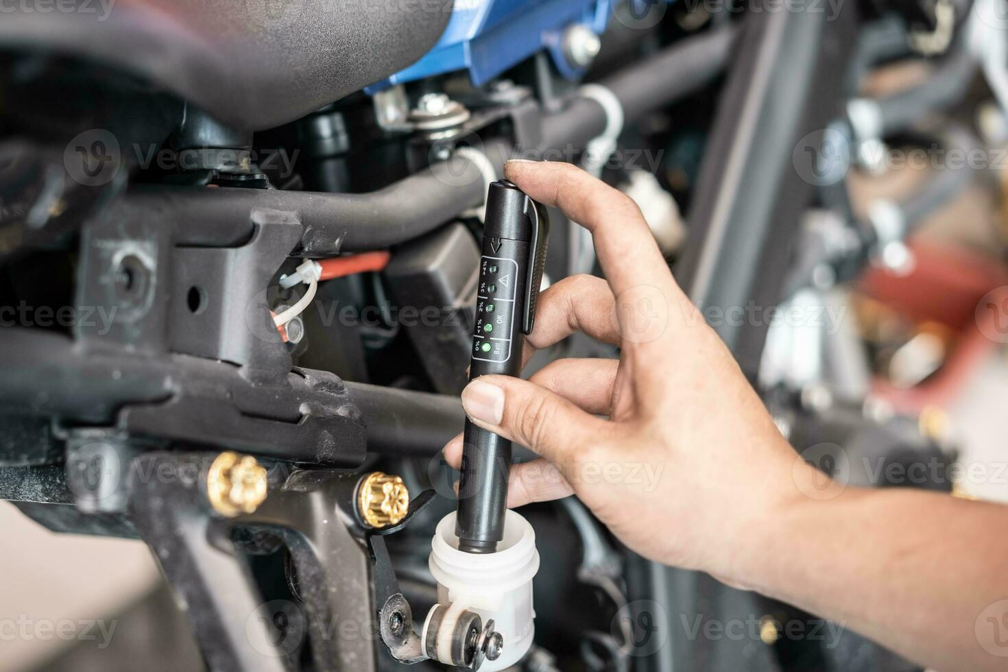 Technician checks brake fluid in motorcycle with Brake Fluid Liquid Tester Quality Check Pen Tool at garage, motorcycle maintenance and repair concept photo