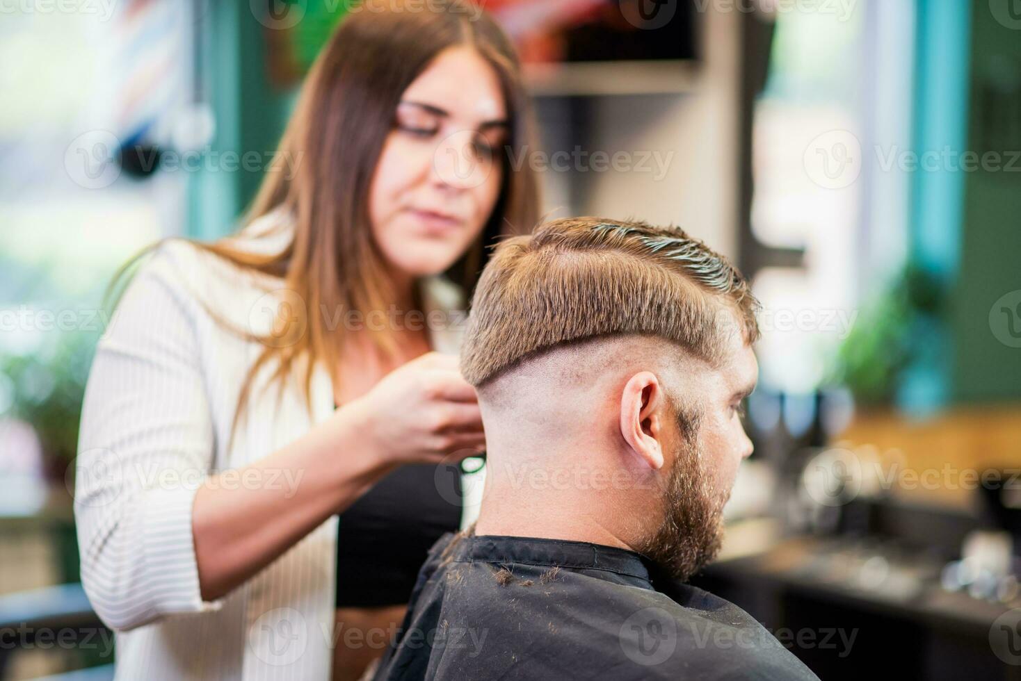 Hairdresser woman cutting hair with clipper man in barbershop photo