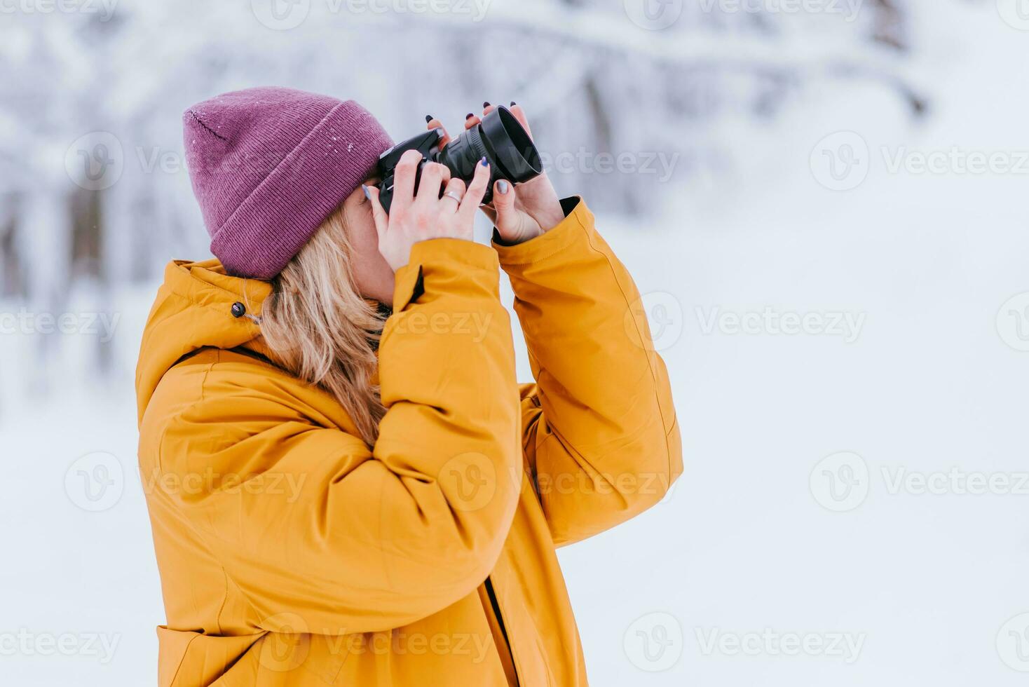 Happy girl photographer in a yellow jacket takes pictures of winter in a snowy park photo