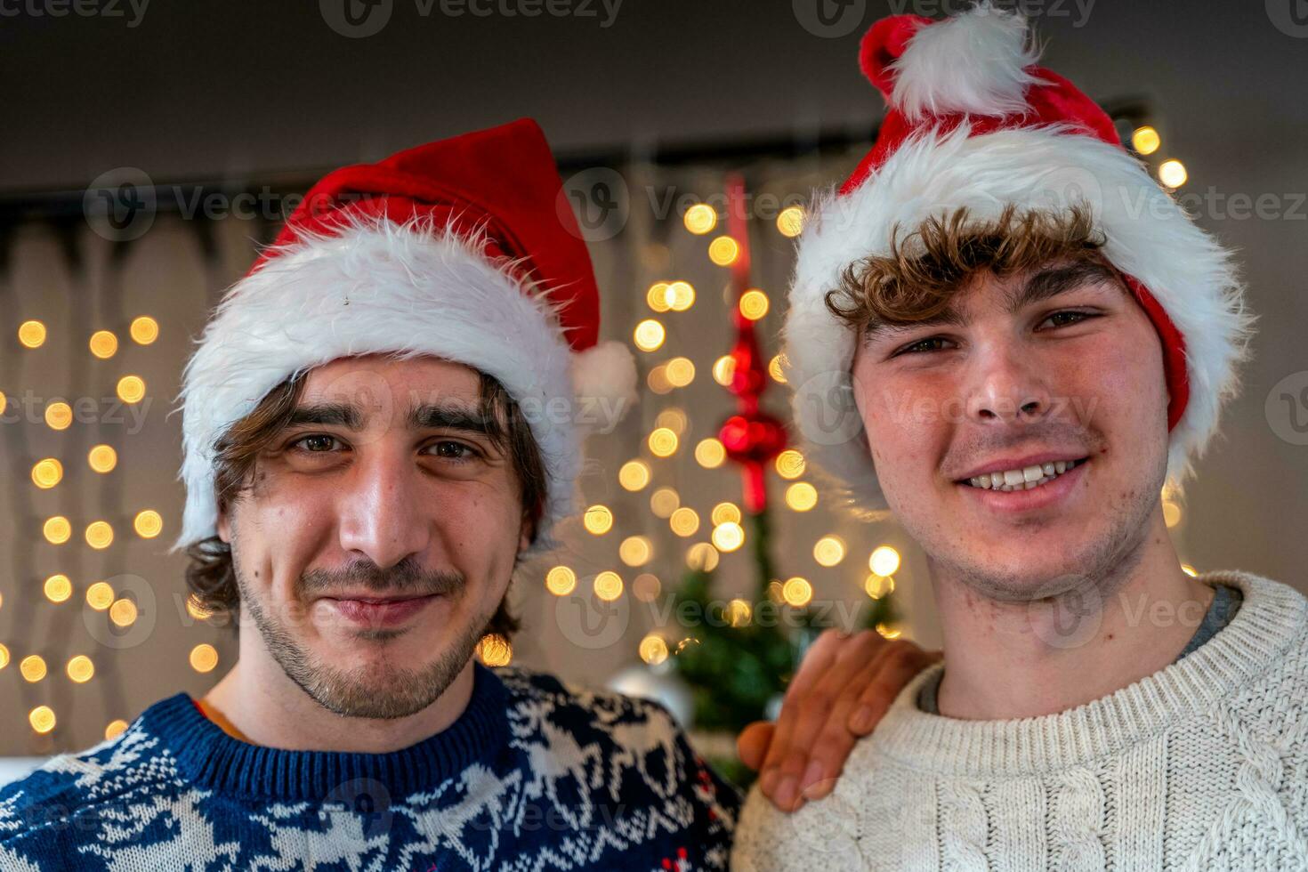 retrato de dos sonriente joven hombres vistiendo rojo sombrero en frente de un pared de Navidad luces foto