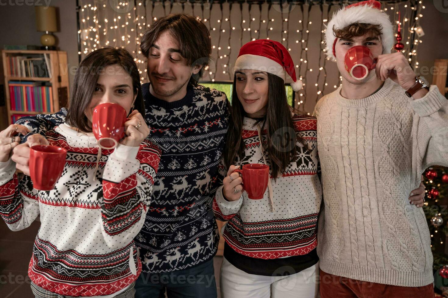 group of four young friends toasting with red cups dressed in red hats and Christmas sweatshirts photo