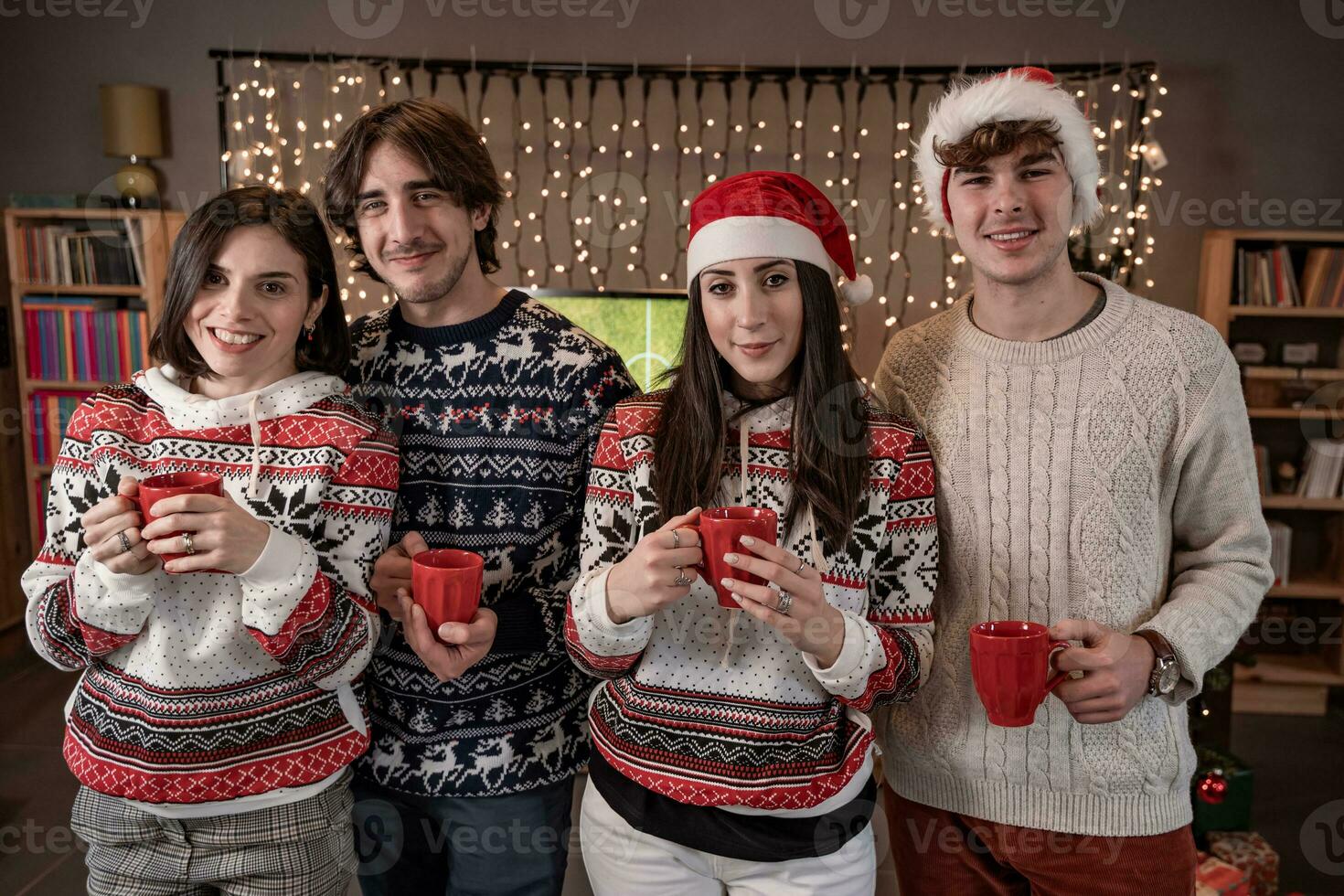 group of four young friends toasting with red cups dressed in red hats and Christmas sweatshirts photo