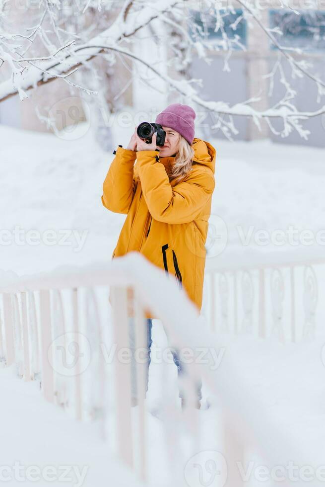 Beautiful girl in a yellow jacket photographer takes pictures of snow in a winter park photo