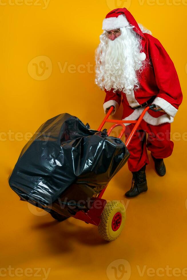 Papa Noel claus es corriendo con un saco lleno de regalos en un metal carretilla en naranja antecedentes foto