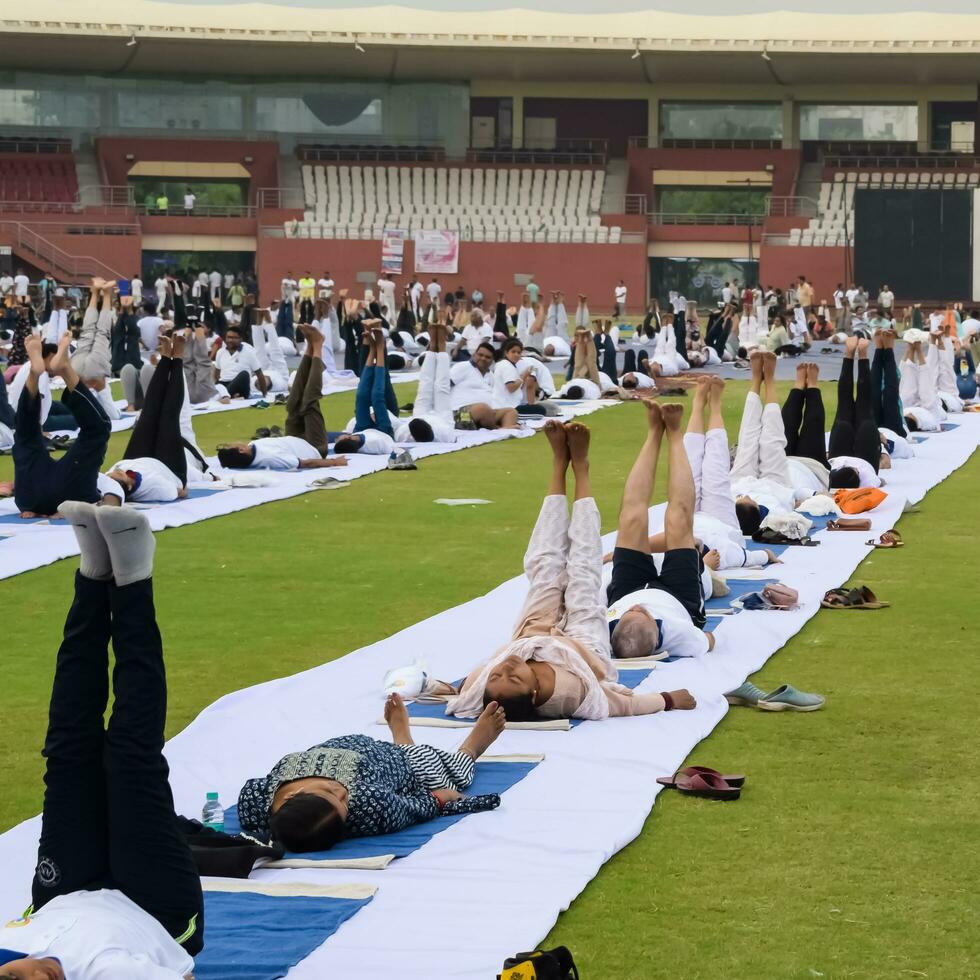 New Delhi, India, June 21, 2023 - Group Yoga exercise session for people at Yamuna Sports Complex in Delhi on International Yoga Day, Big group of adults attending yoga class in cricket stadium photo