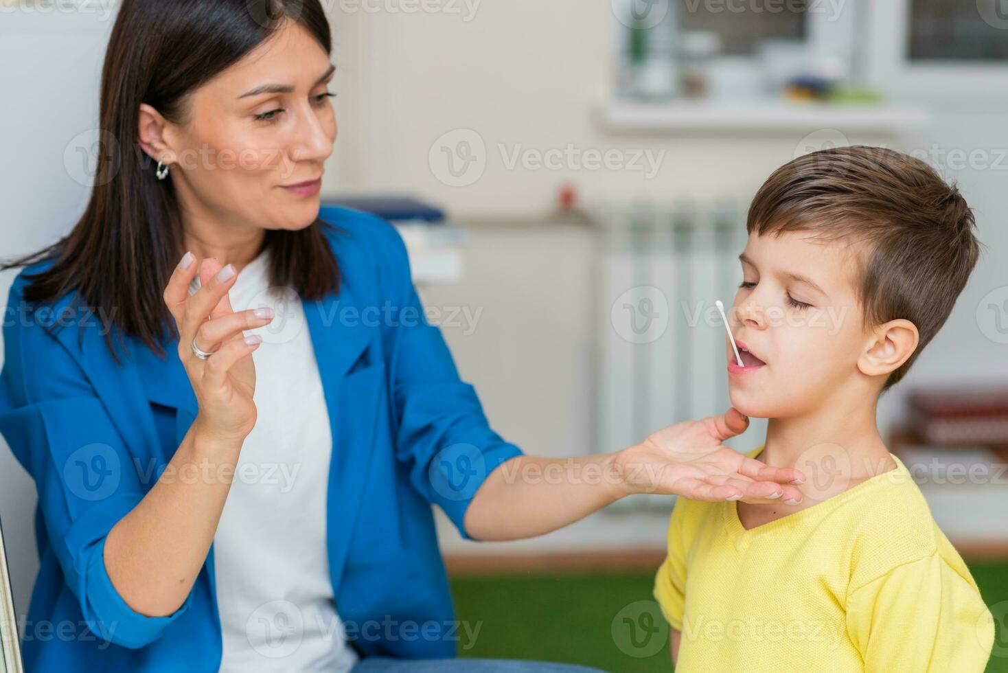 Woman speech therapist corrects speech defects in a boy in her office photo