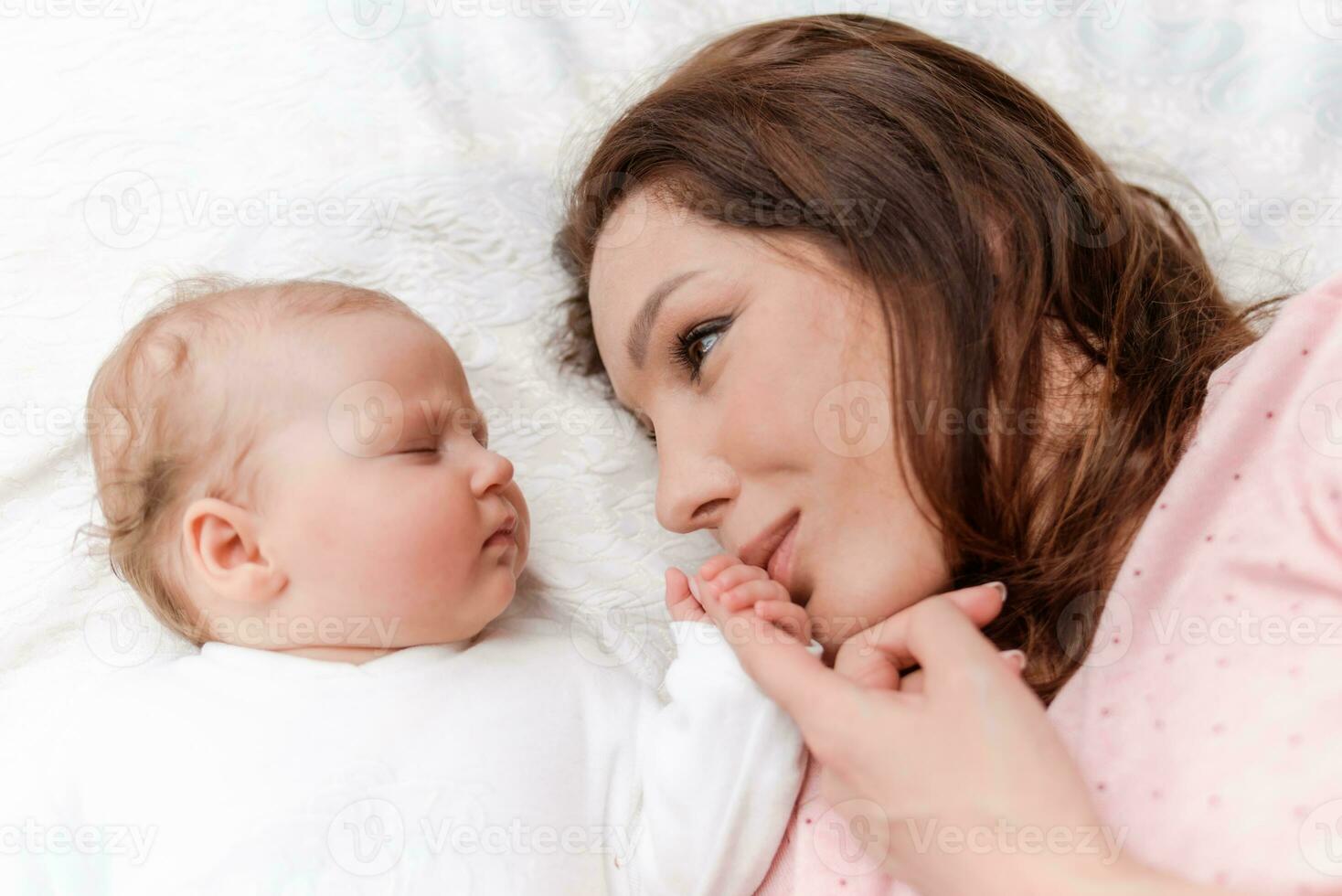 Young beautiful woman holding small hand of her sleeping baby daughter in bedroom photo