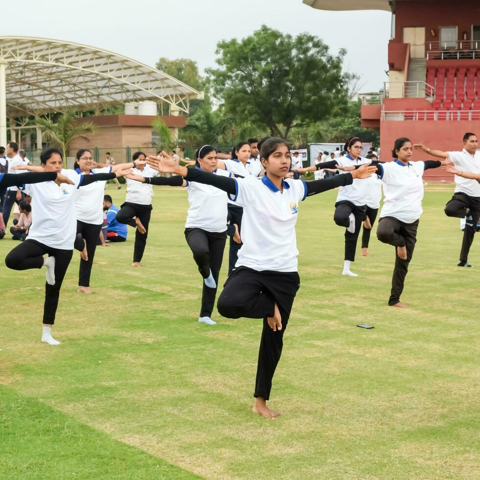 New Delhi, India, June 21, 2023 - Group Yoga exercise session for people at Yamuna Sports Complex in Delhi on International Yoga Day, Big group of adults attending yoga class in cricket stadium photo