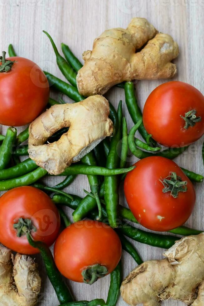 Fresh Ginger, Tomato and green chili pepper on plain wooden table, green essential vegetables for all essential foods, view of unpeeled vegetables with plain background photo