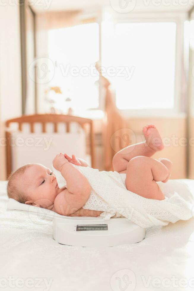 Happy baby lying on the scales in the bedroom photo