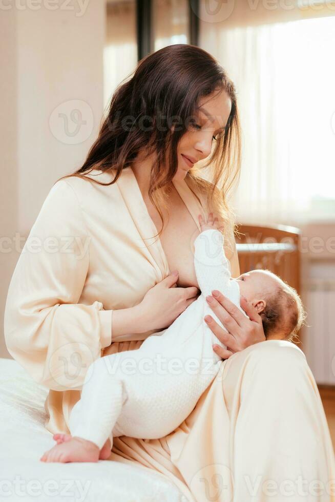 Young woman feeding her baby with milk from the breast in the bedroom while sitting on the bed photo