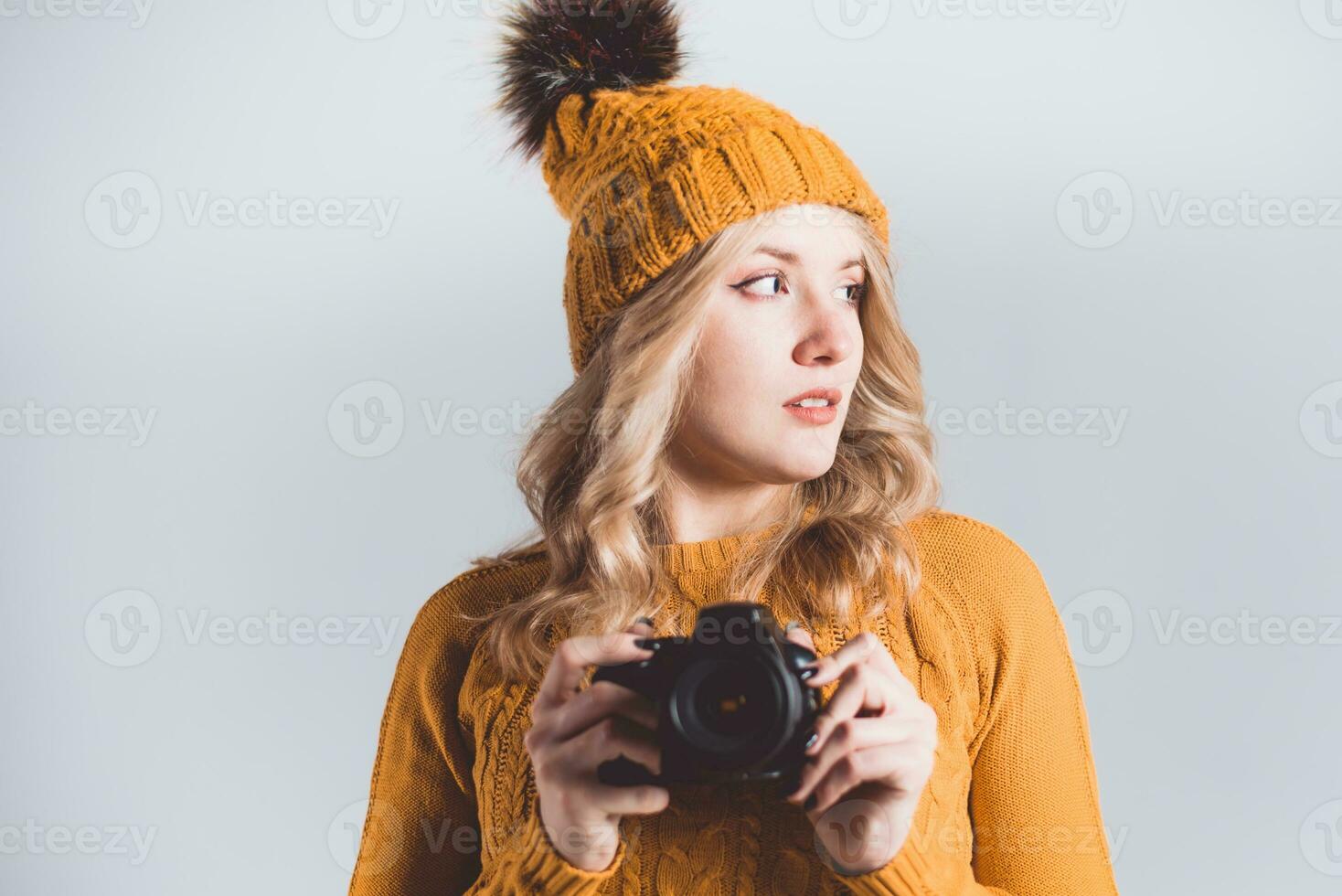 Beautiful girl photographer in a knitted hat posing with a camera in her hands in a photo studio