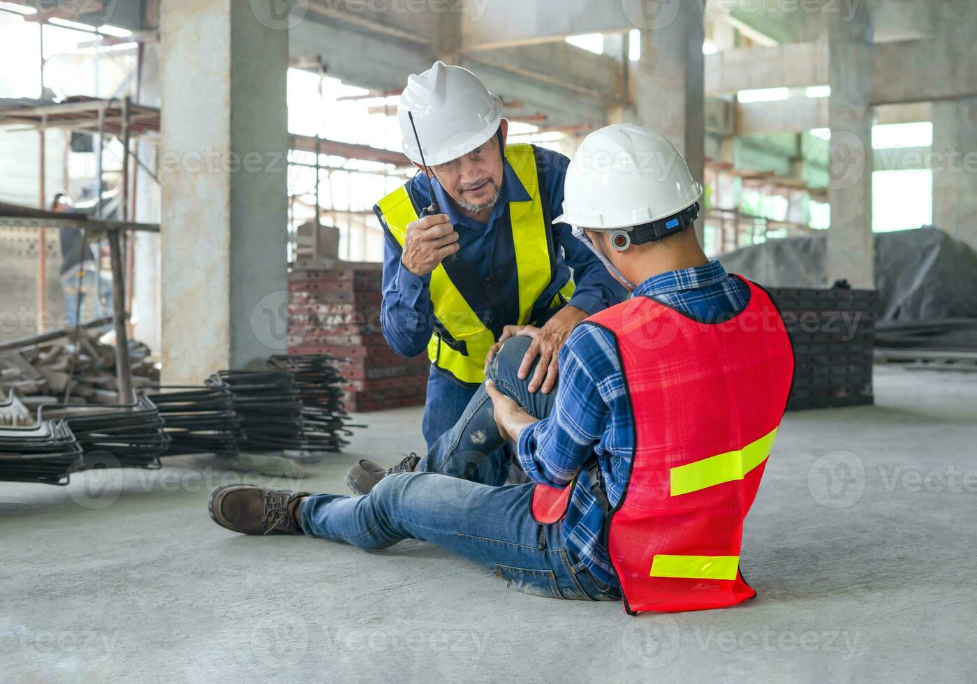 un trabajador vestir la seguridad engranaje estaba lesionado sentado en piso a sitio, un colega rescatado él desde accidente, usando walkie-talkie a llamada primero ayuda concepto de equipo de riesgo gestión, accidente en sitio trabajo foto