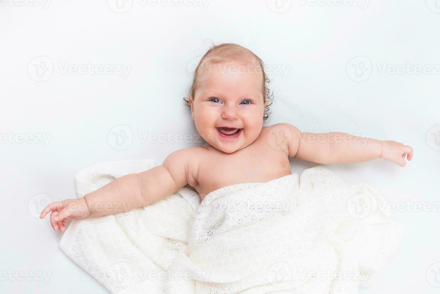 Cute happy baby lies on a white sheet and is covered with a woolen cloth photo