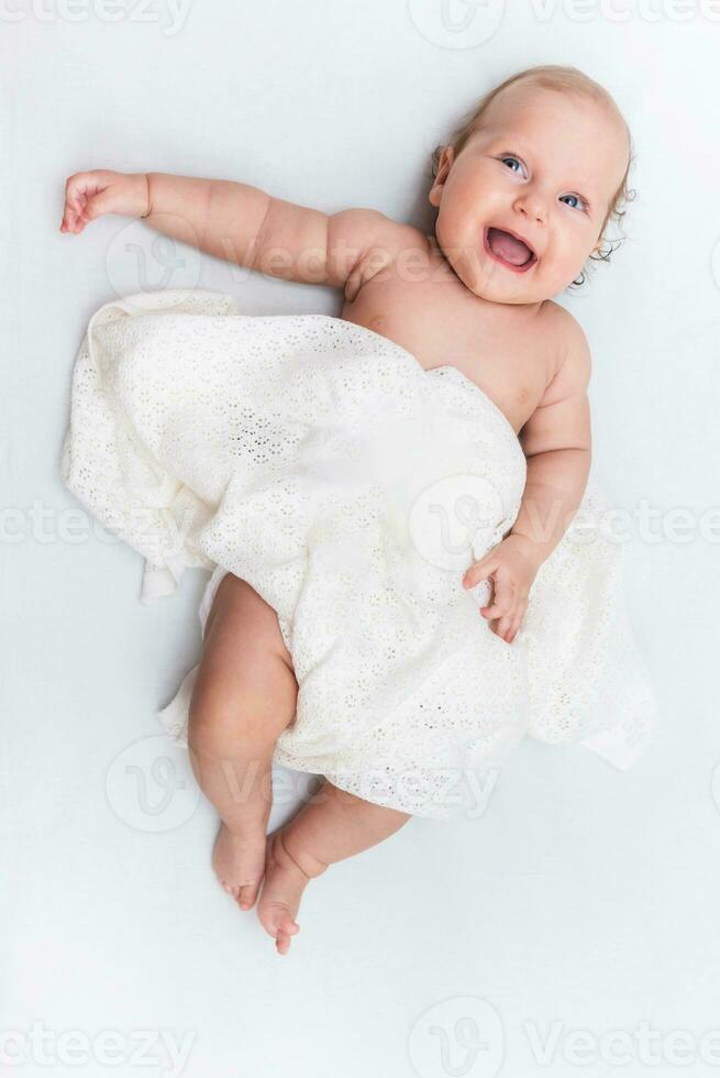 Laughing baby girl who lies on a white sheet and is covered with a woolen cloth photo