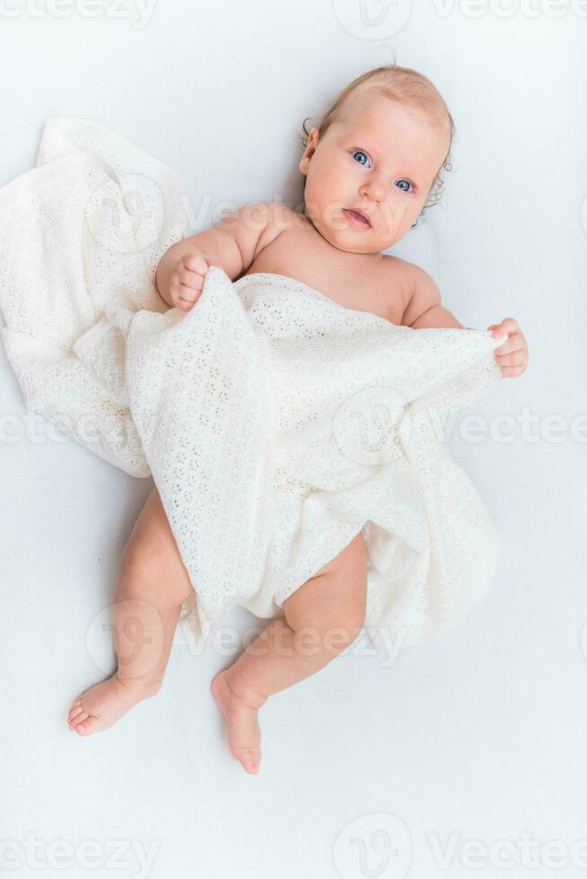 Portrait of a beautiful baby girl lies on a white sheet in her room photo