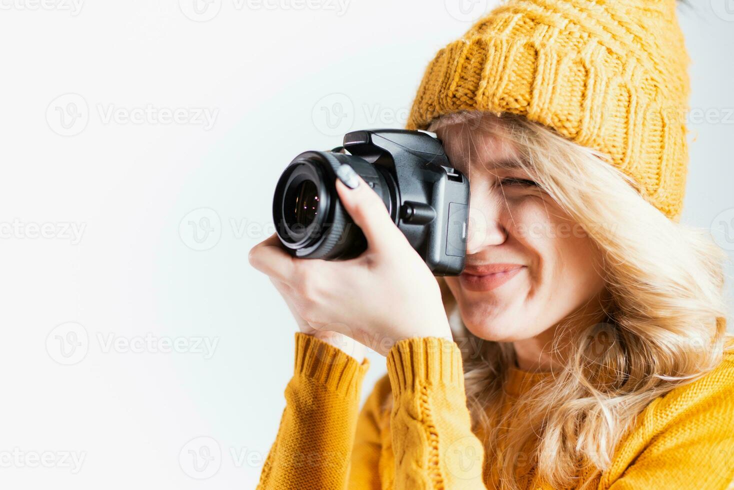 Beautiful girl photographer in a knitted hat posing with a camera in her hands in a photo studio