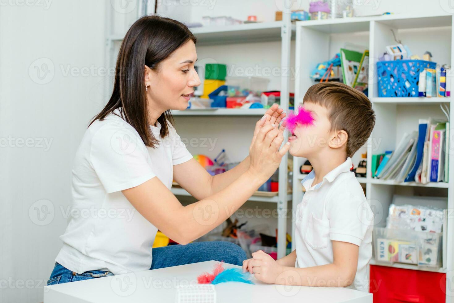 un mujer habla terapeuta enseña un niño a soplar correctamente en de colores plumas. foto