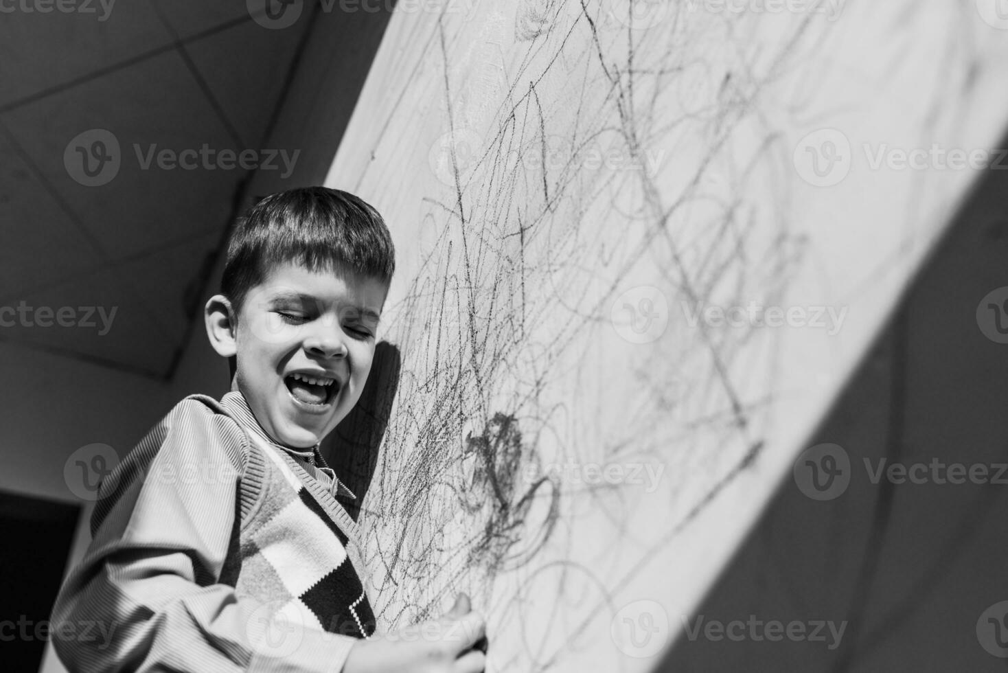 Laughing child draws on the wall with chalk in his room. The boy is engaged in creativity at home. Black and white photo