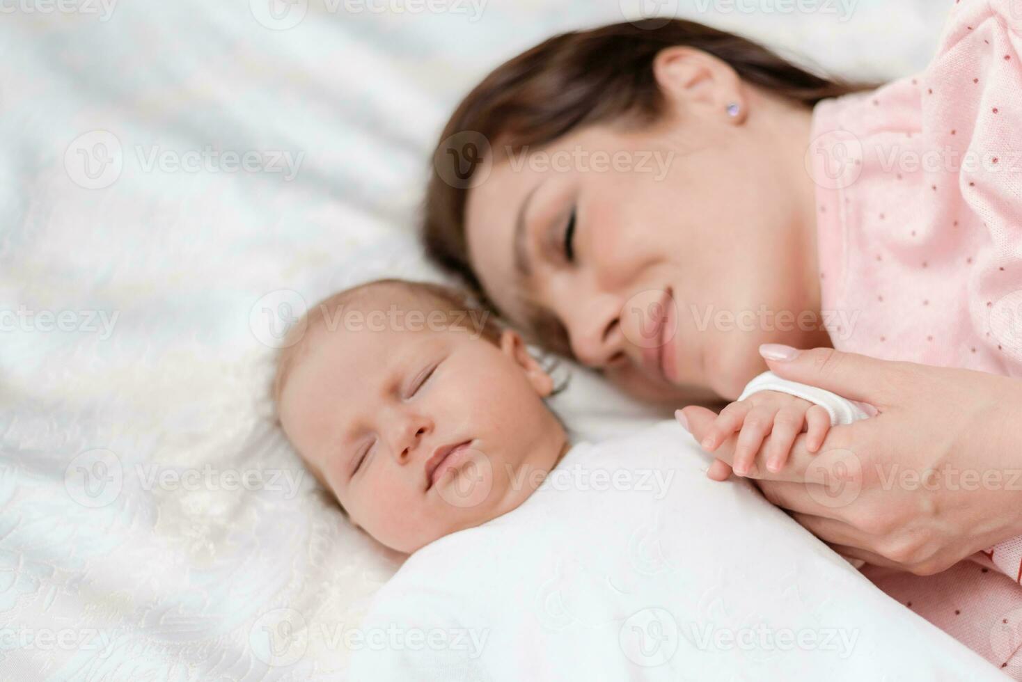 Young beautiful woman holding small hand of her sleeping baby daughter in bedroom photo