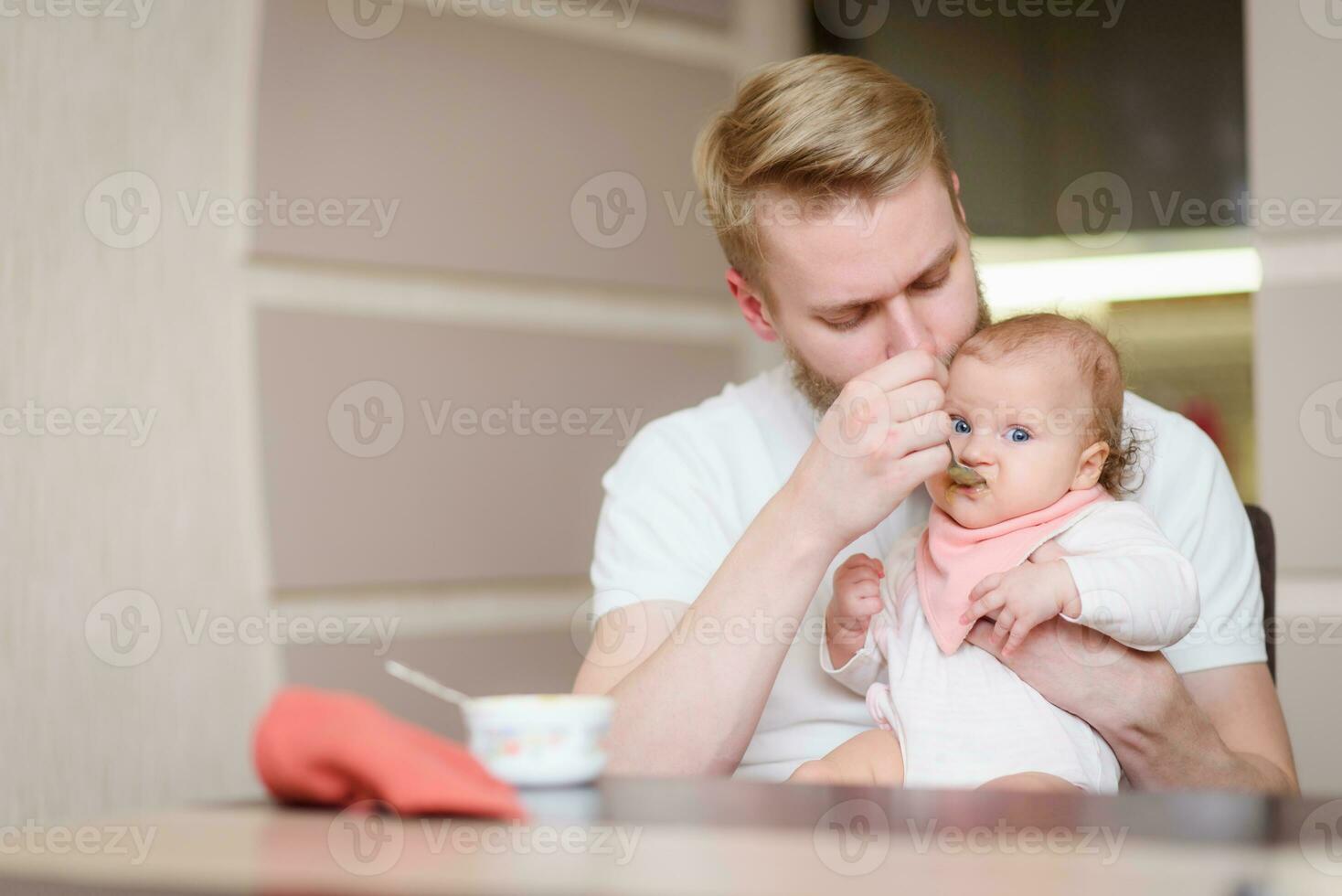 Father feeding his daughter fruit puree in the kitchen photo