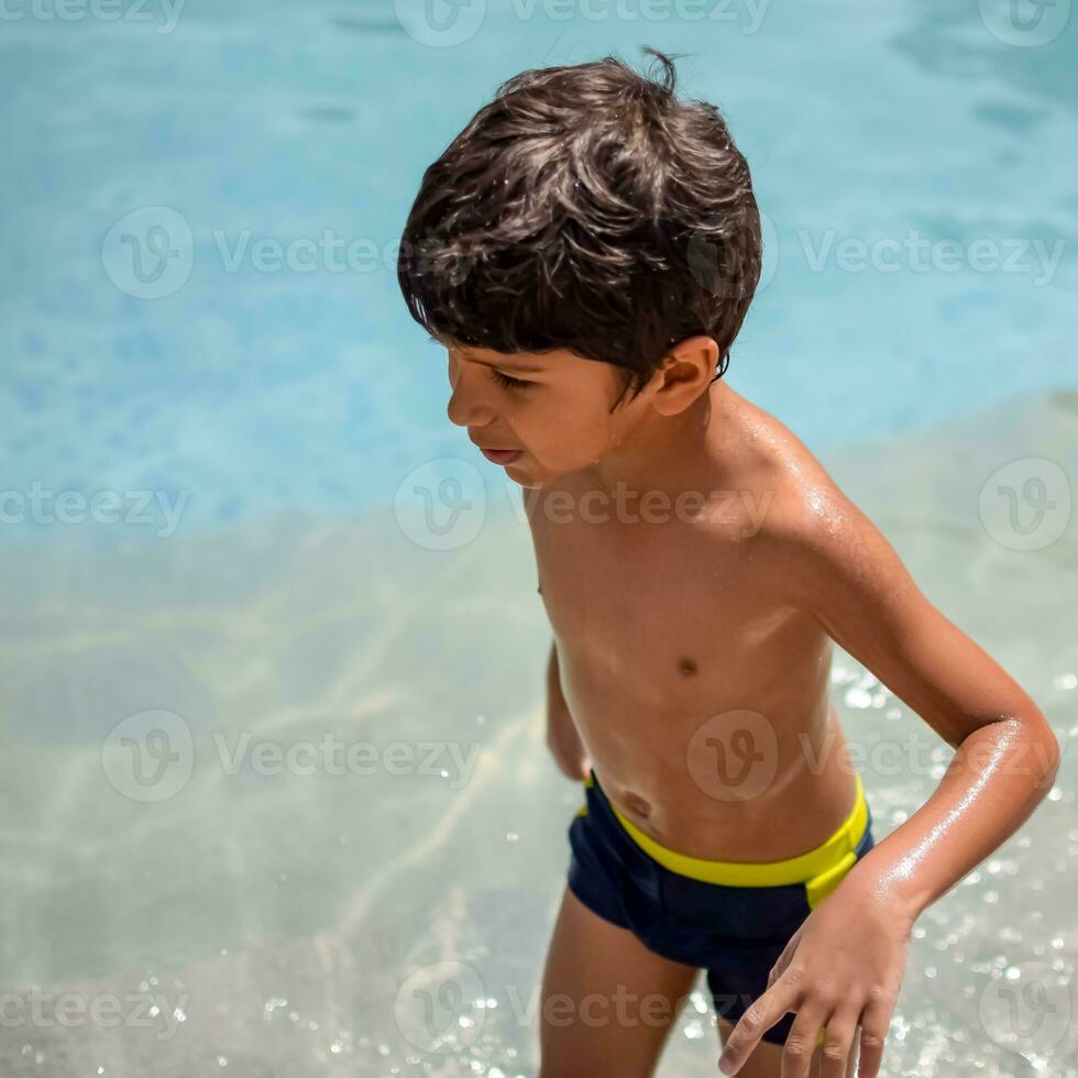 contento indio chico nadando en un piscina, niño vistiendo nadando disfraz a lo largo con aire tubo durante caliente verano vacaciones, niños chico en grande nadando piscina. foto