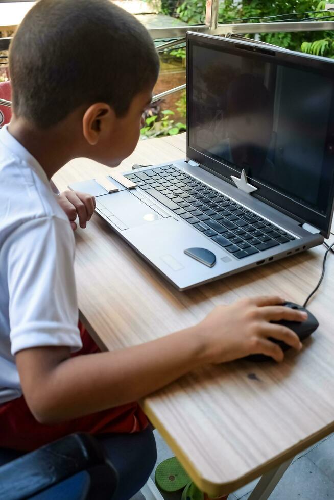 Little boy sitting at table using laptop for online class in Grade 1, Child studying on laptop from home for distance learning online education, School boy children lifestyle concept photo