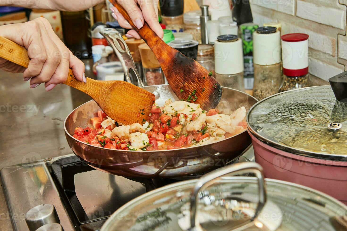 Pieces of chicken breast with tomatoes are fried in frying pan on gas stove photo