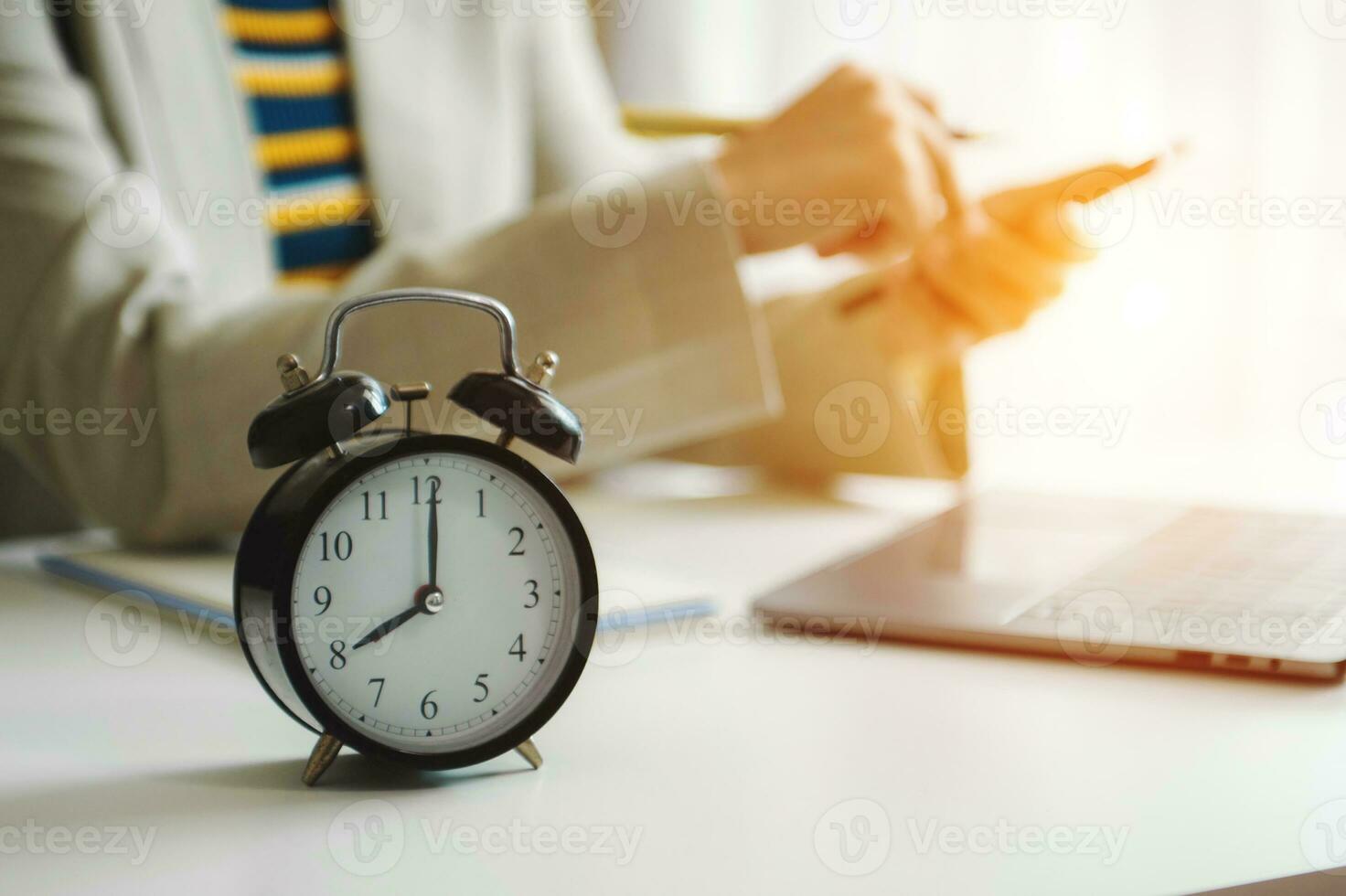 Alarm clock on the desk. Business hand using smartphone, laptop and tablet  working in modern office building photo