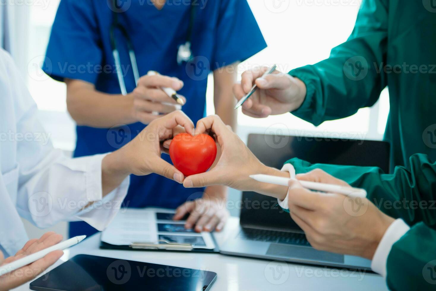 Medical team having a meeting with doctors in white lab coats and surgical scrubs seated at a table discussing a patients working online using computers photo