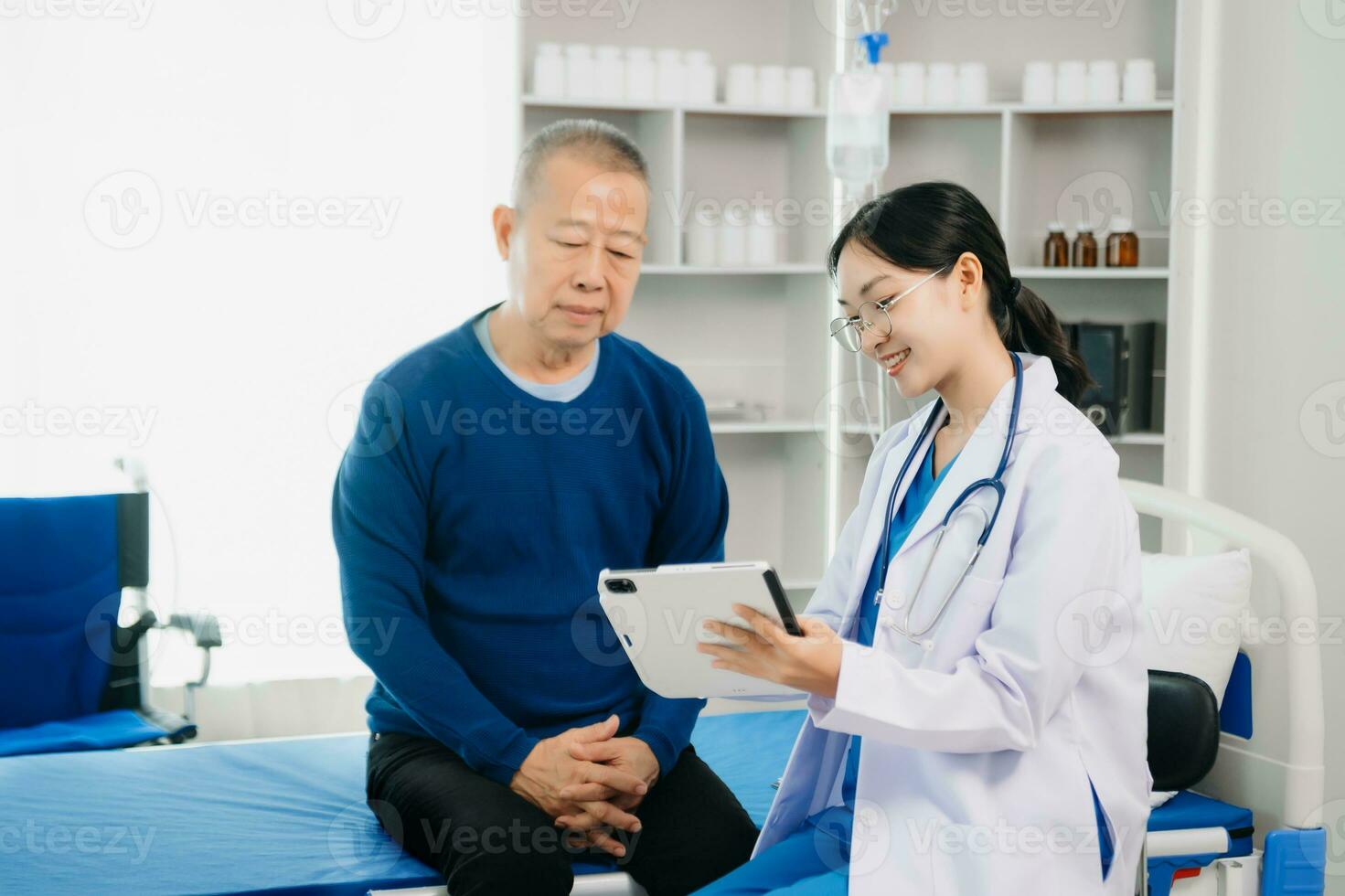 médico que se discute tratamiento con mayor masculino paciente hablando y riendo sentado en examen cama en clínica o hospital foto