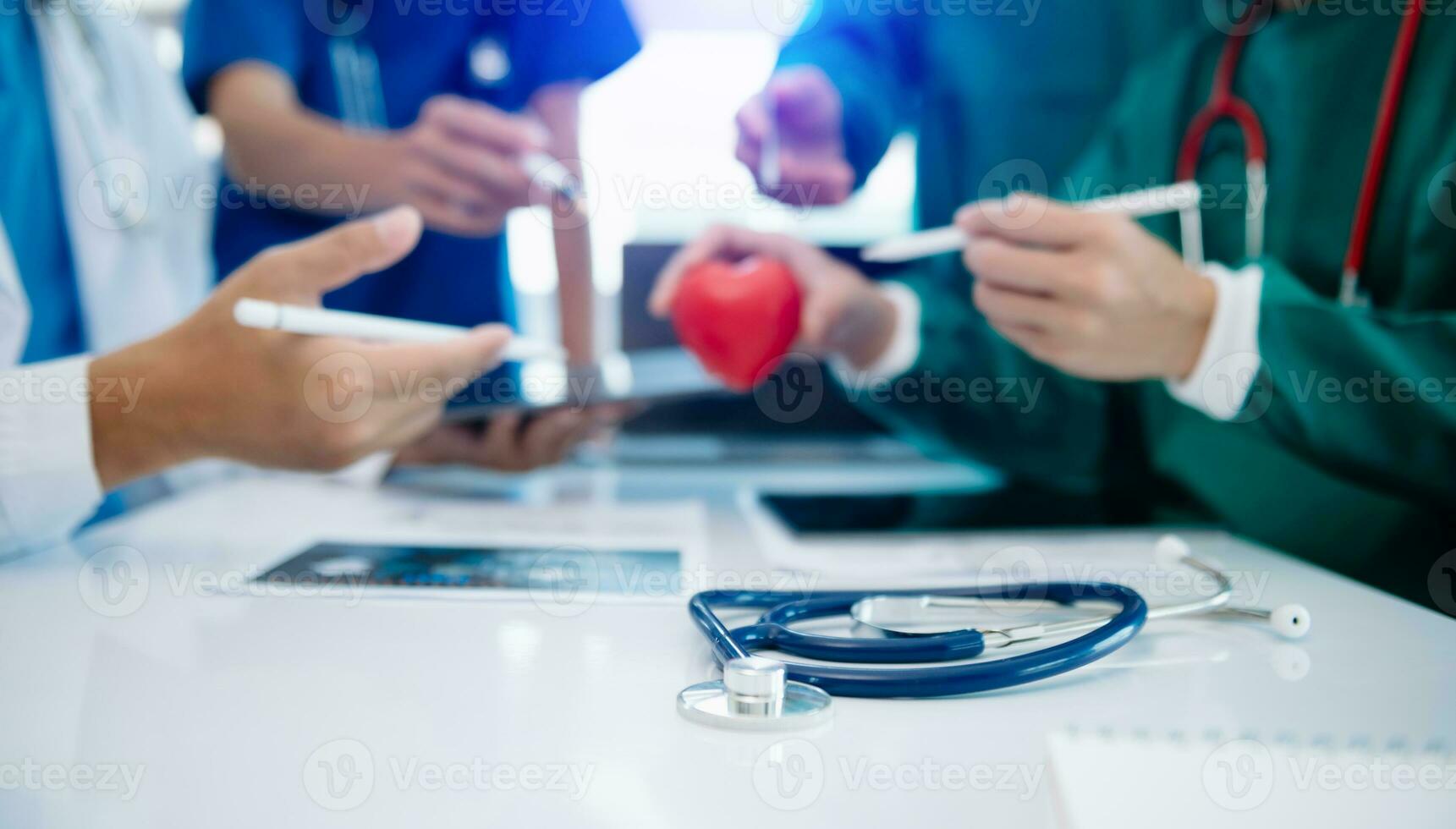 Medical team having a meeting with doctors in white lab coats and surgical scrubs seated at a table discussing a patients working online using computers photo