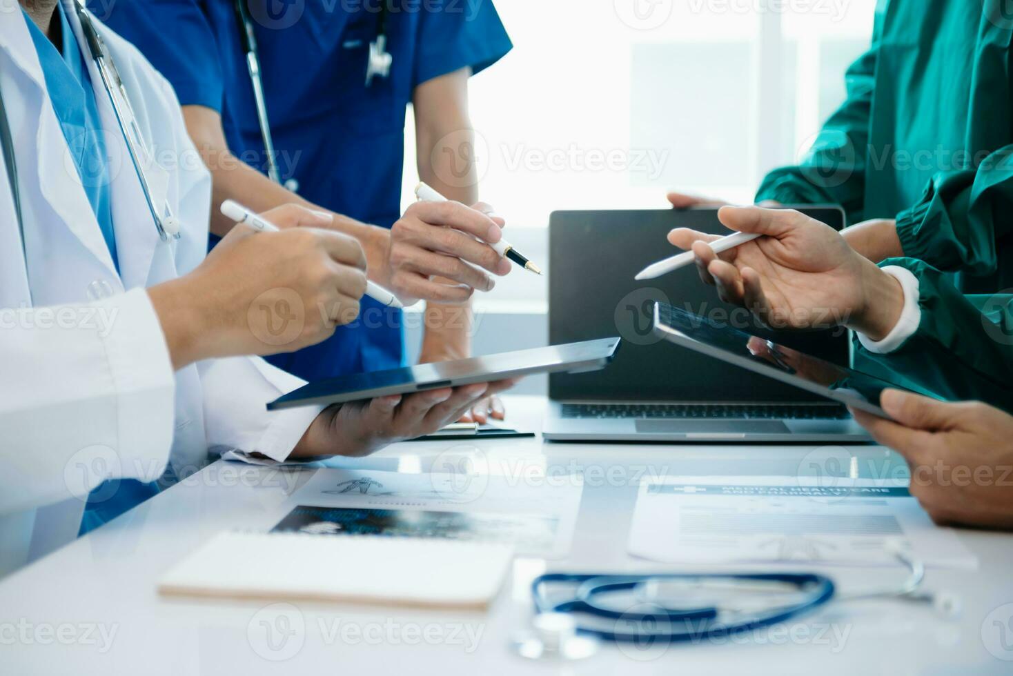 Medical team having a meeting with doctors in white lab coats and surgical scrubs seated at a table discussing a patients working online using computers photo