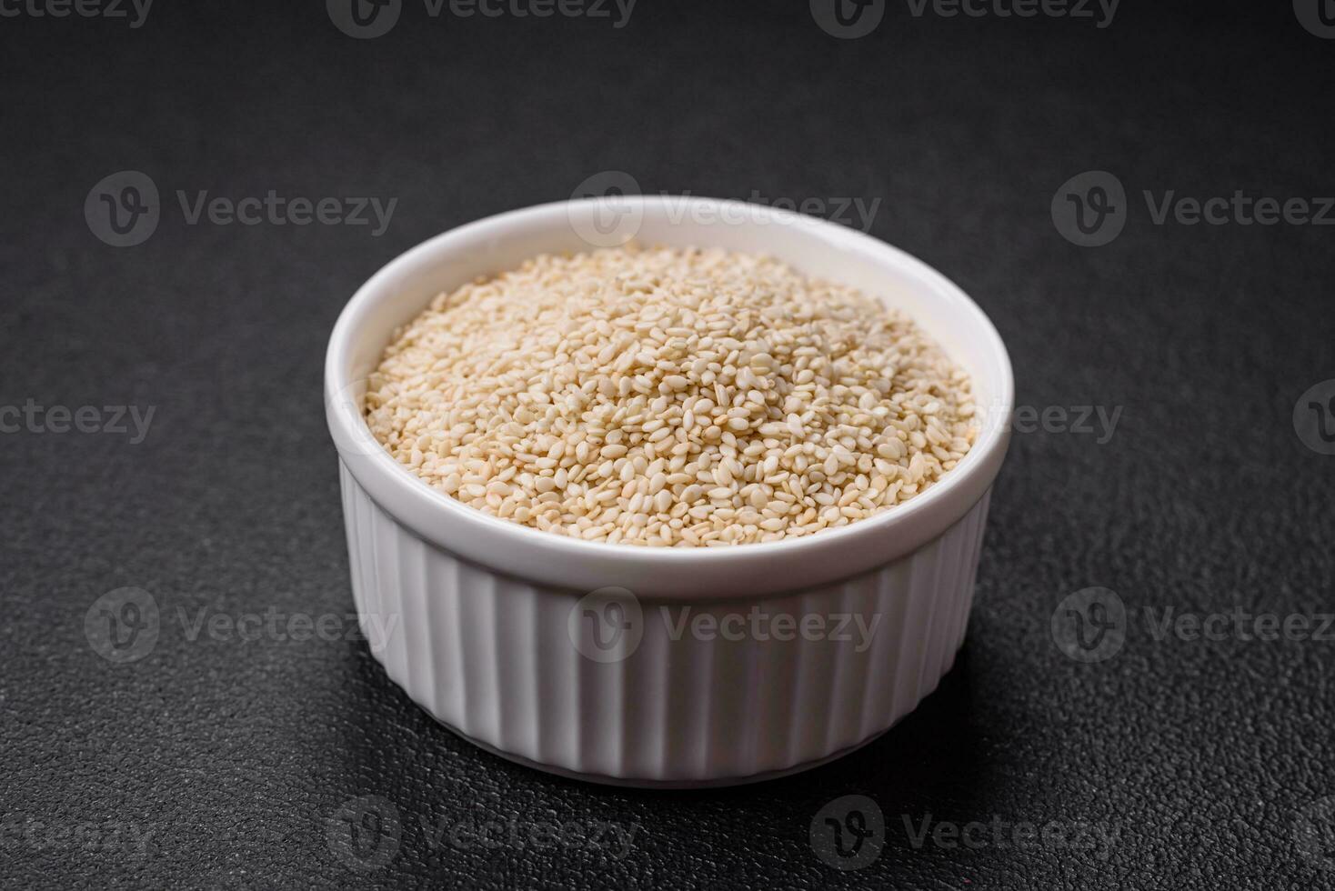 Raw white sesame seeds or grains in a bowl on a textured concrete background photo