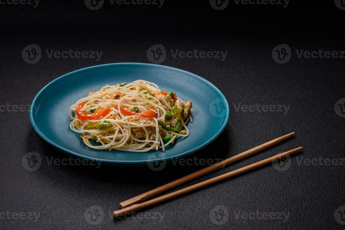 Tasty dish of Asian cuisine with rice noodles, chicken, asparagus, pepper, sesame seeds photo