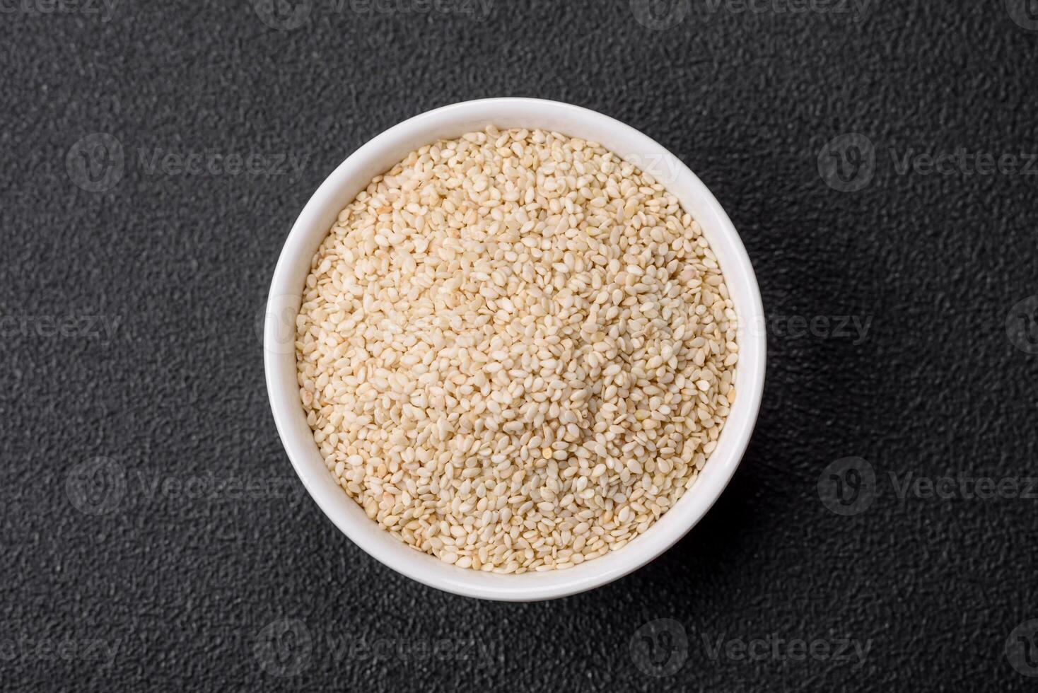 Raw white sesame seeds or grains in a bowl on a textured concrete background photo