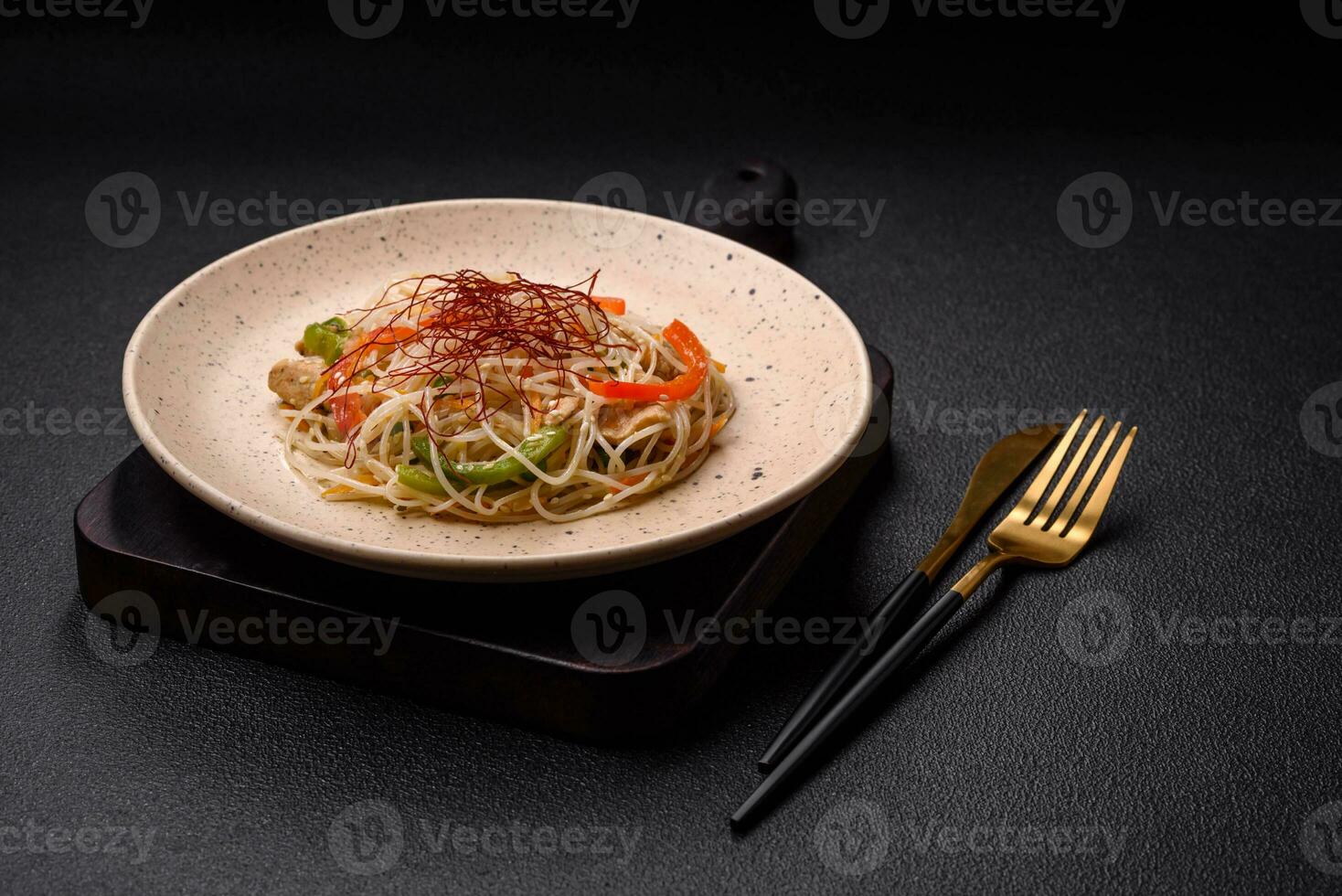 Tasty dish of Asian cuisine with rice noodles, chicken, asparagus, pepper, sesame seeds photo