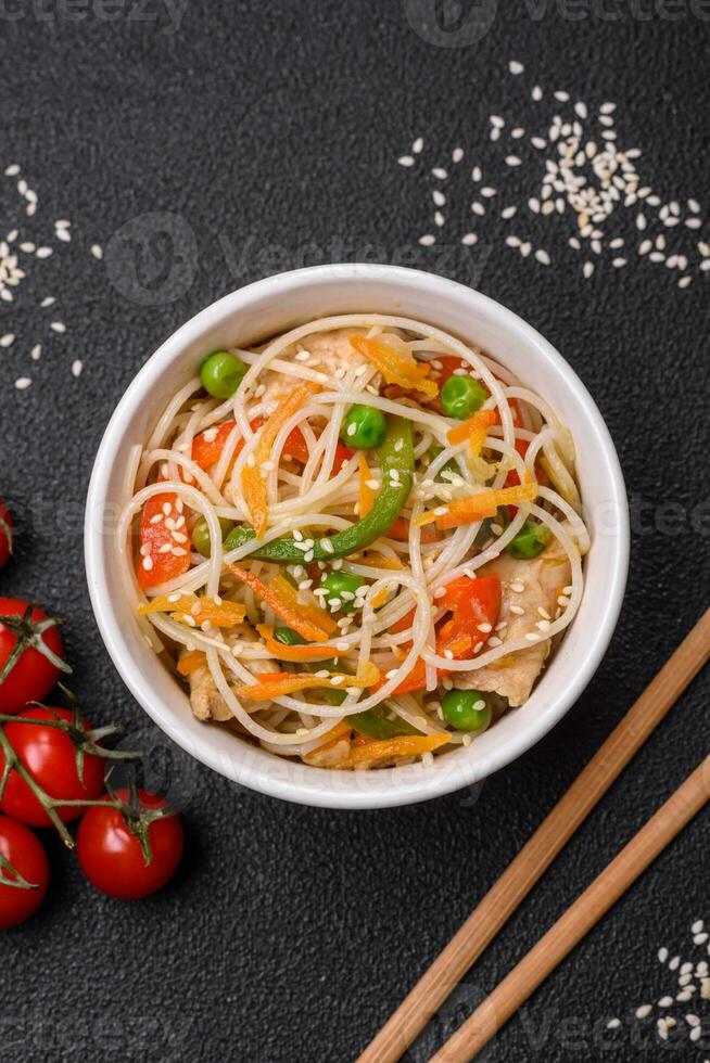 Tasty dish of Asian cuisine with rice noodles, chicken, asparagus, pepper, sesame seeds photo